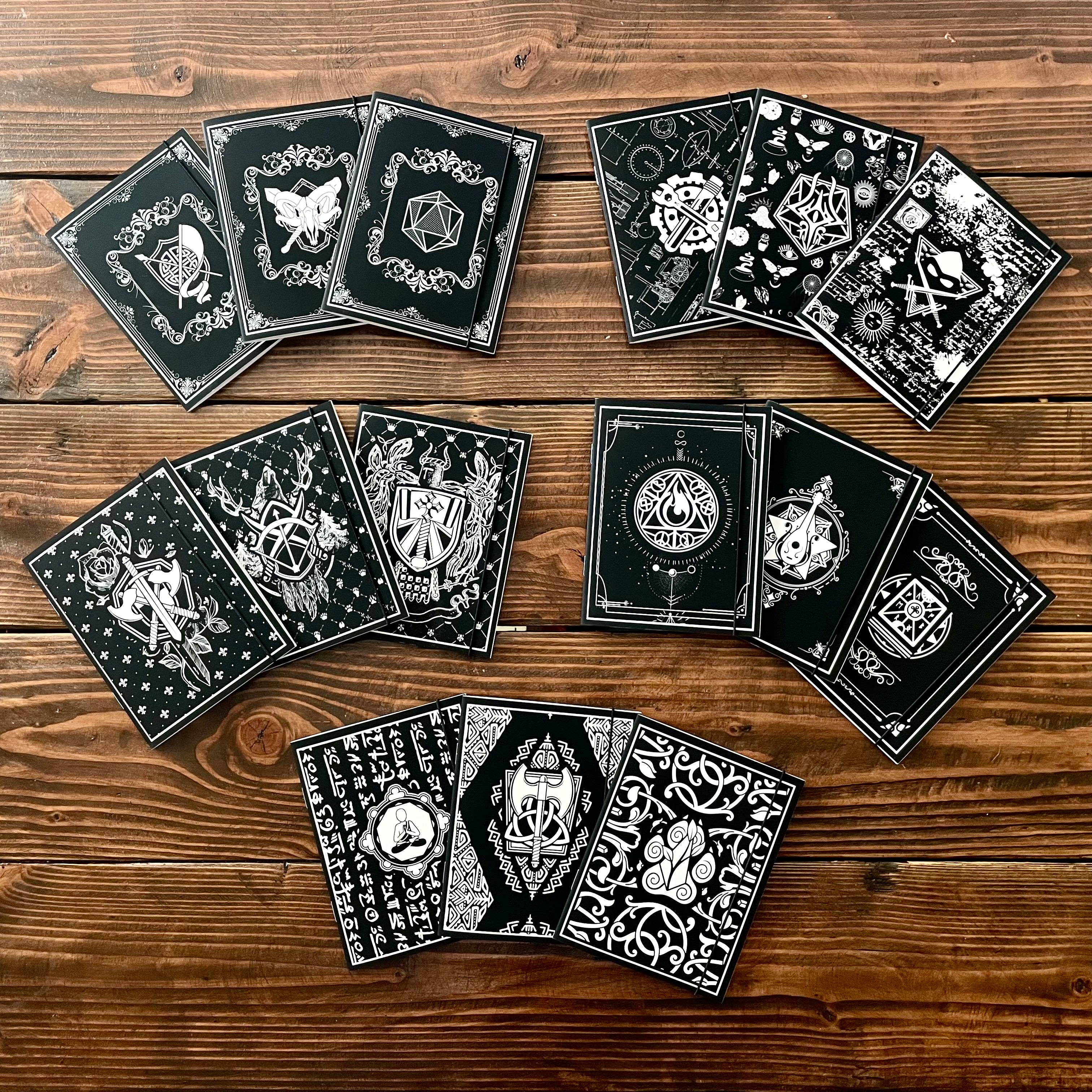 Class Cover 5E Character Journals - Set of black and white character journals with fantasy-themed illustrations on wooden surface.