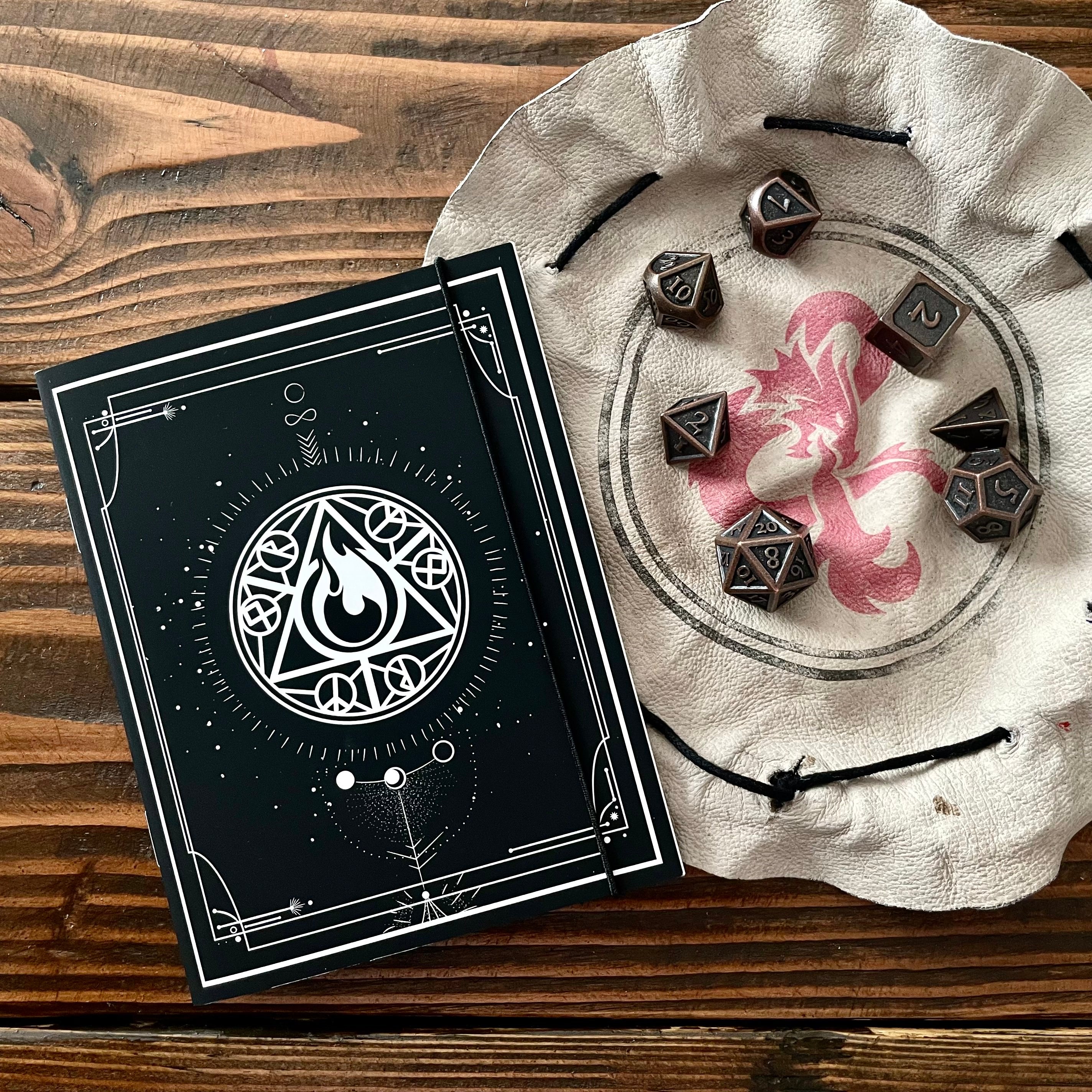 Class Cover 5E Character Journals - Black DnD journal with white arcane symbol design next to beige drawstring pouch holding black polyhedral dice with silver.