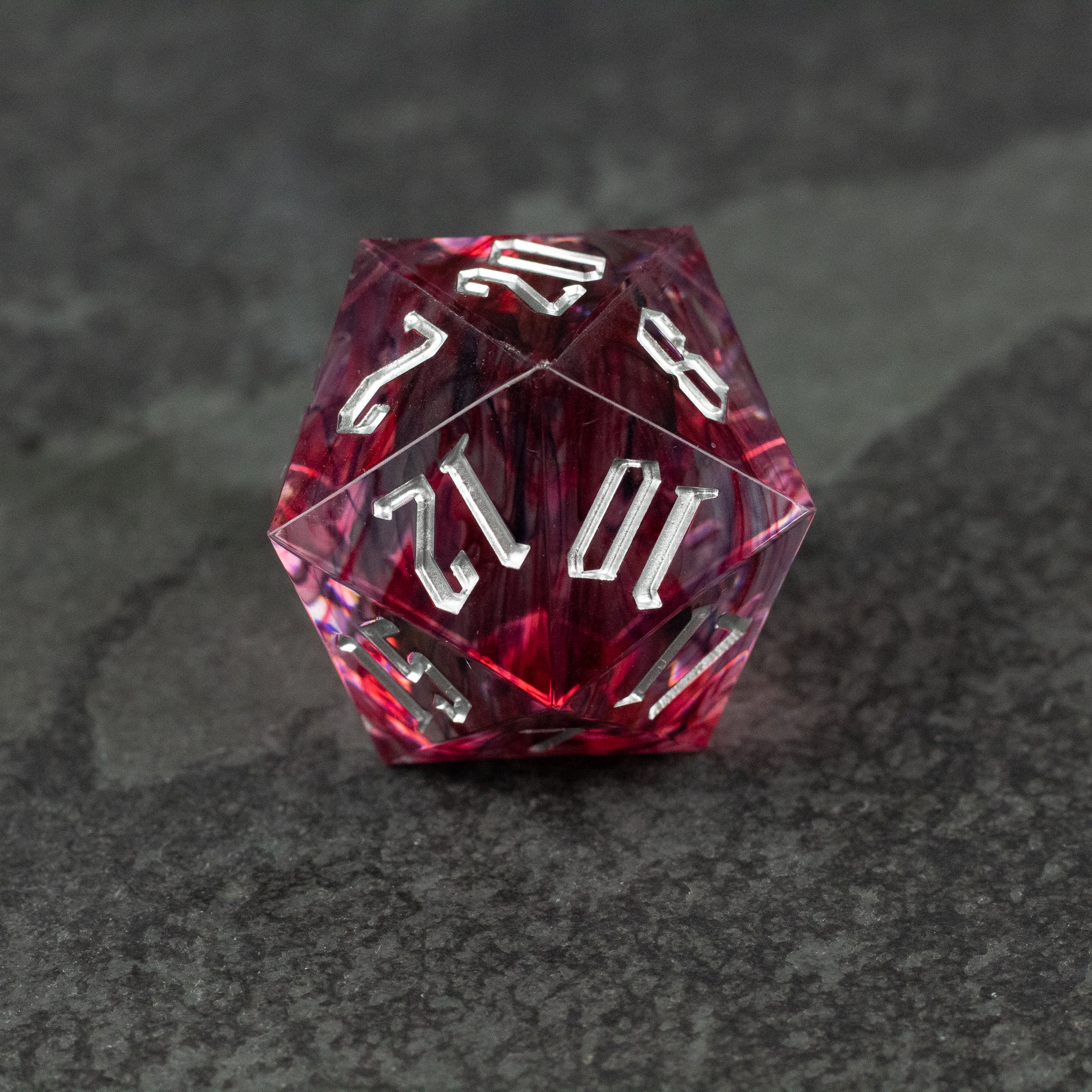 33mm Red Swirl D20 - 33mm translucent red swirl d20 dice with white numbering on a dark textured surface.