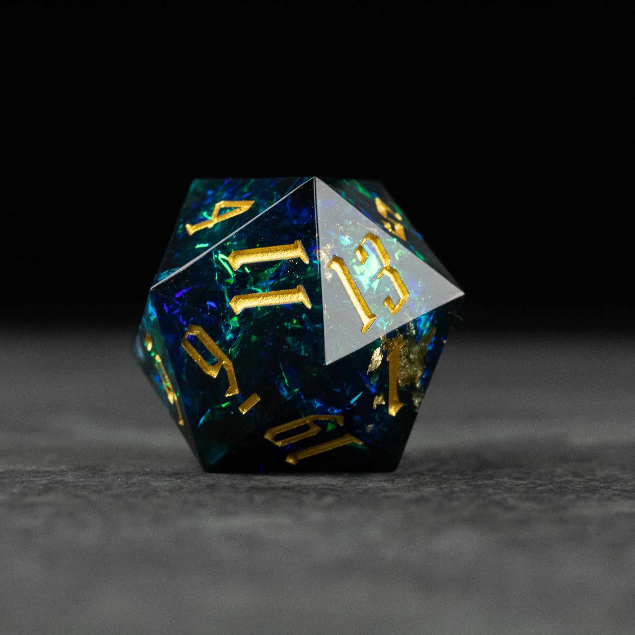 33mm Blue Shimmer D20 - 33mm blue translucent d20 dice with gold shimmer numbers and flecks on gray surface.