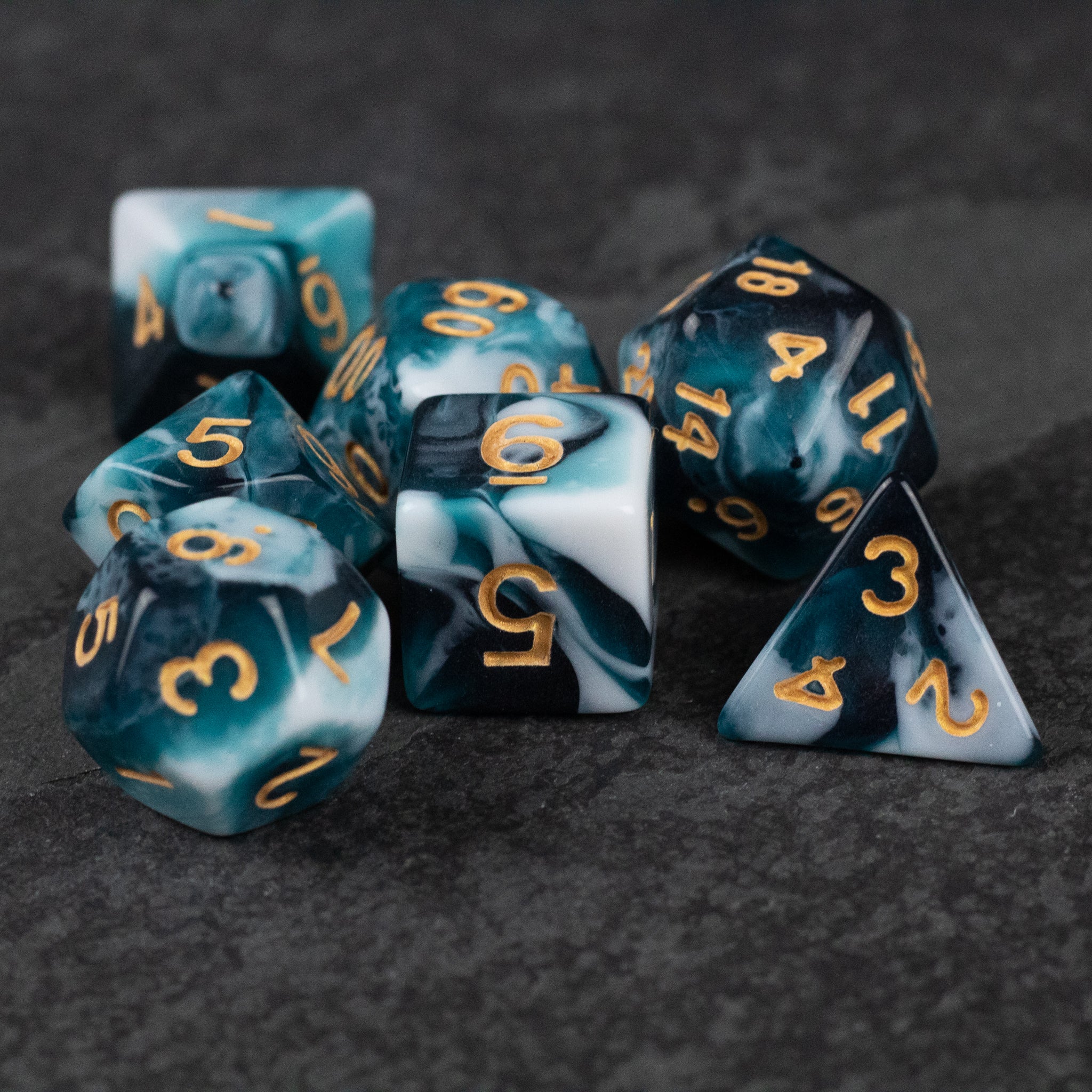 White and Teal Marbled Dice Set - Seven white and teal marbled polyhedral dice with gold numbers on a dark surface.
