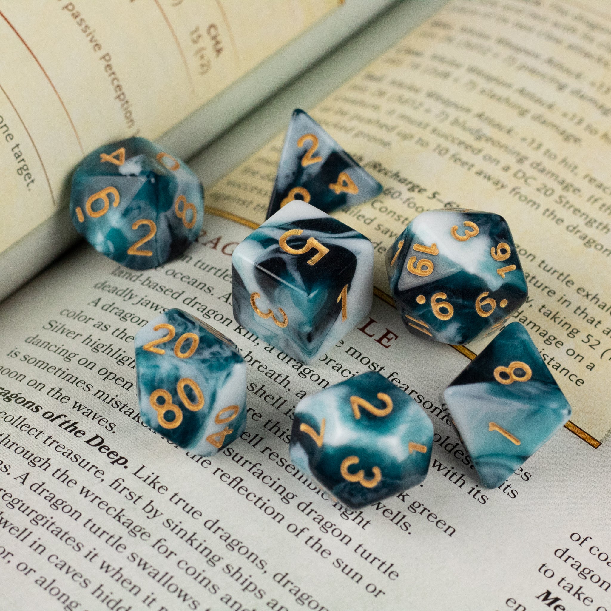 White and Teal Marbled Dice Set - Seven white and teal marbled polyhedral dice with orange numbers on an open book.