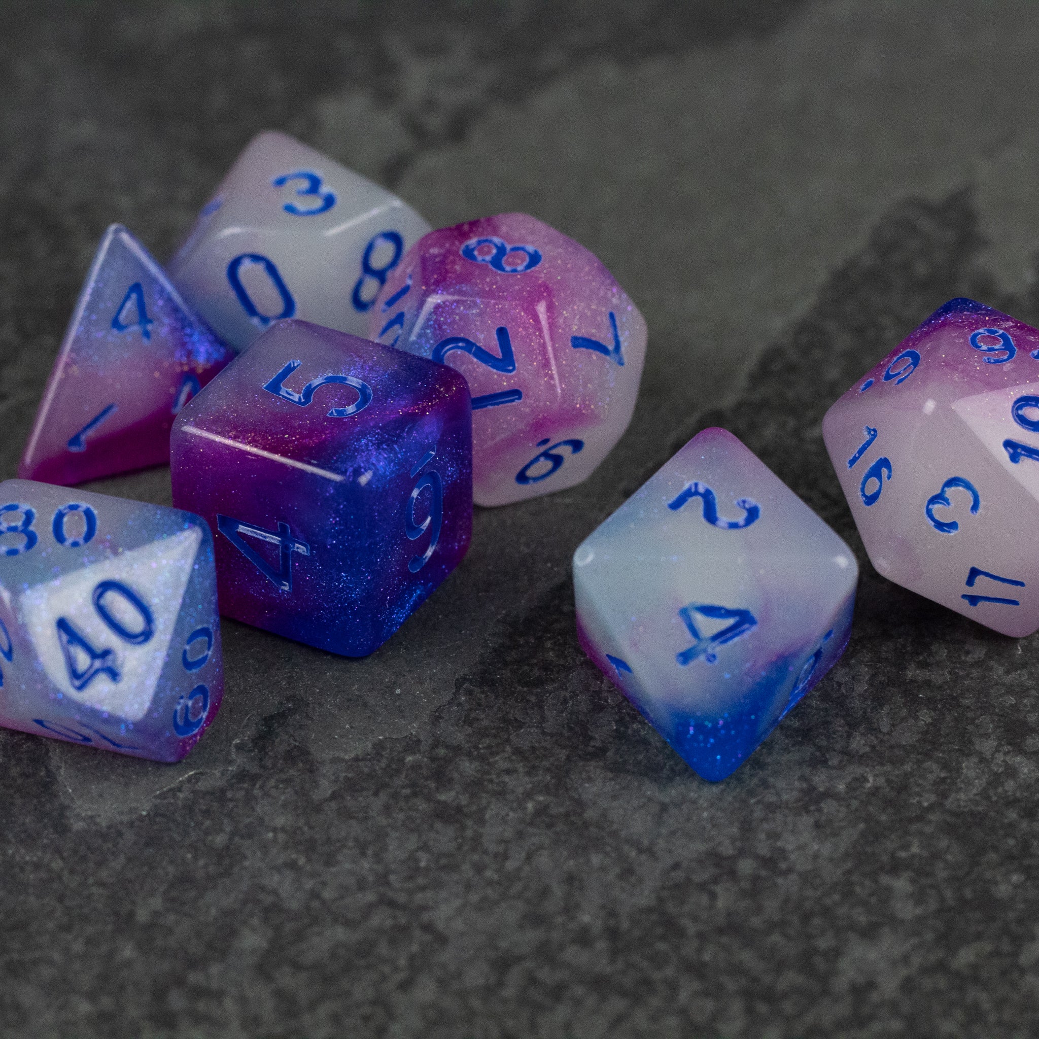 Emberlight Twilight Glow-in-the-Dark Dice Set - Set of seven polyhedral dice with a purple and blue gradient, translucent material, and blue numbers.