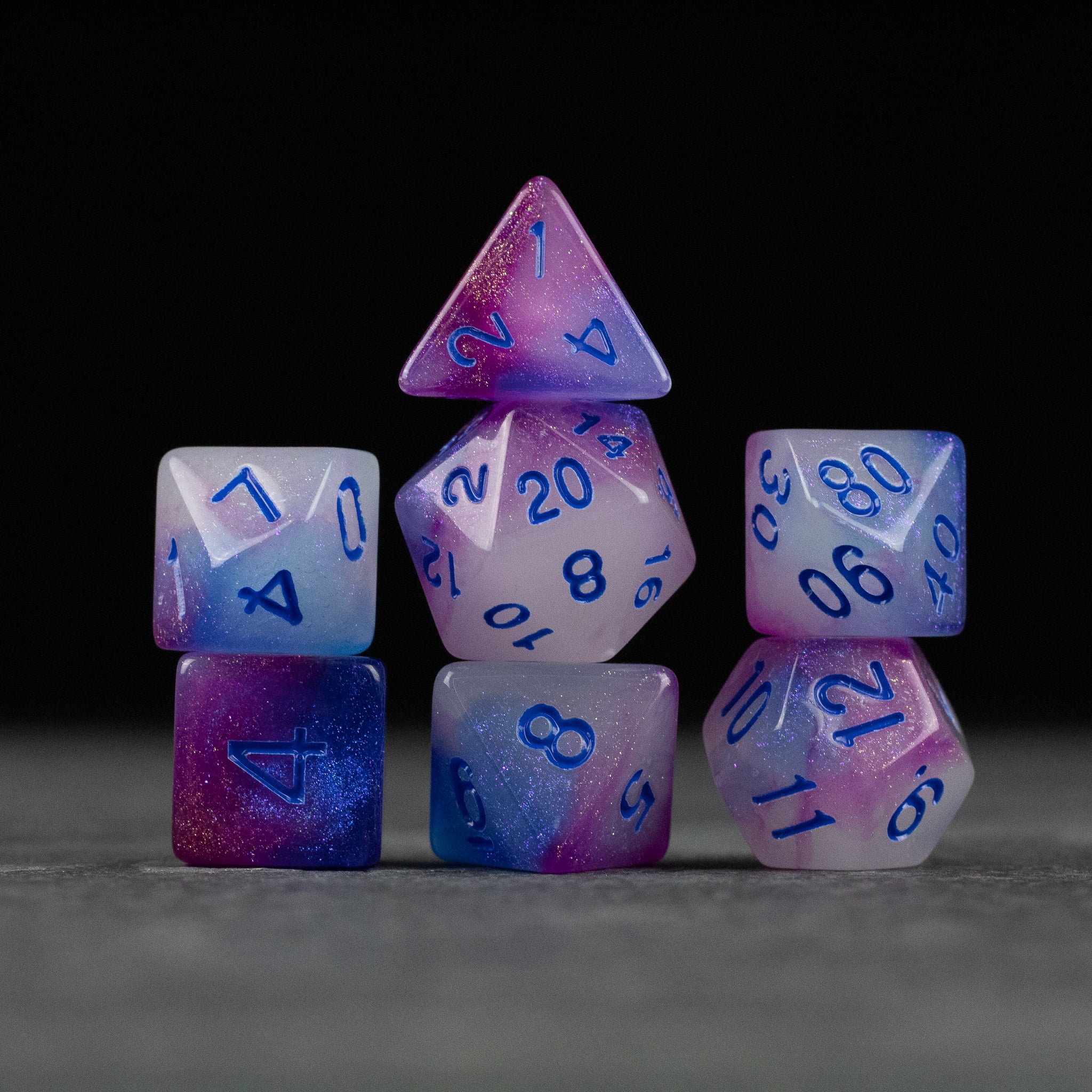 Emberlight Twilight Glow-in-the-Dark Dice Set - Set of seven multi-sided gaming dice in purple, blue, and white gradient with blue numbers, glowing effect.
