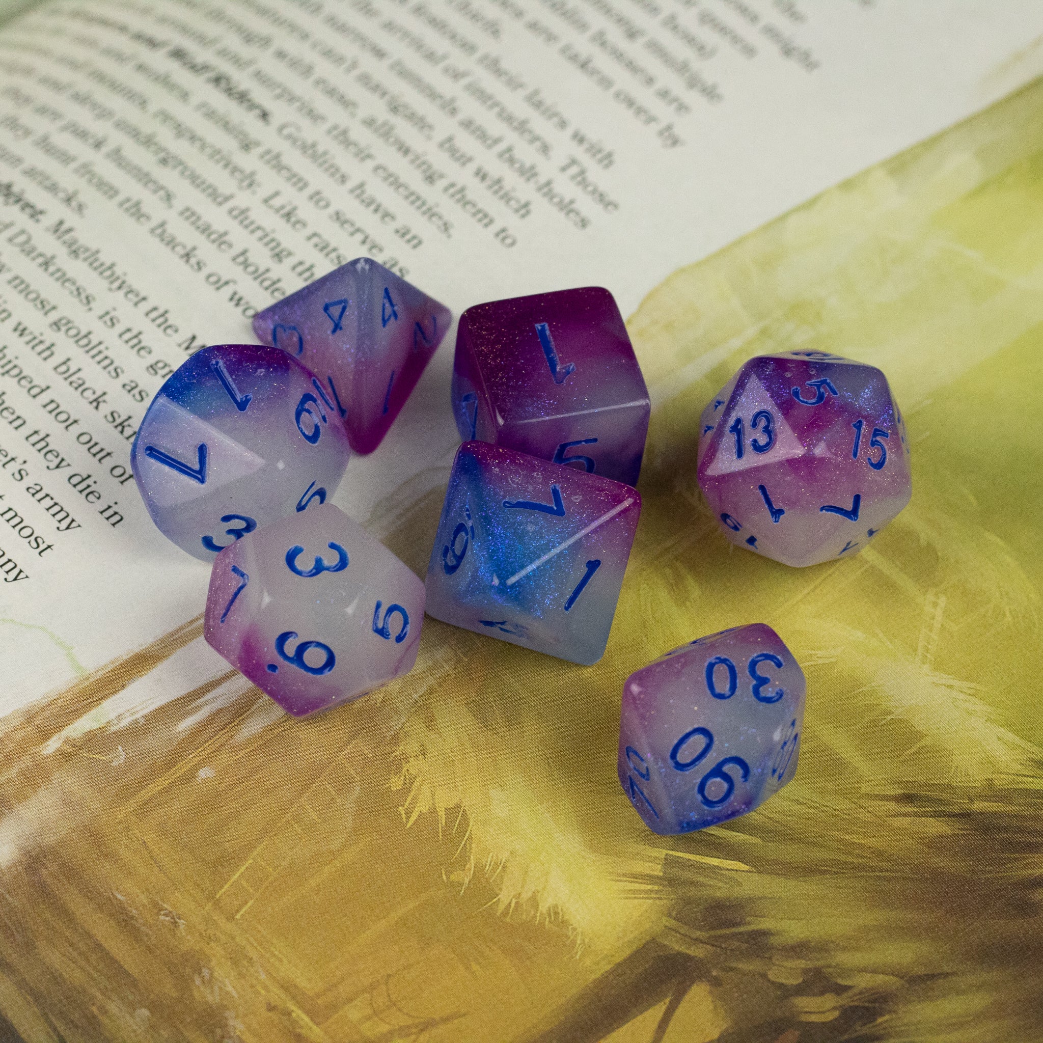 Emberlight Twilight Glow-in-the-Dark Dice Set - Set of seven translucent polyhedral dice in gradient hues of purple and blue with dark blue numbering, glowing subtly on a.