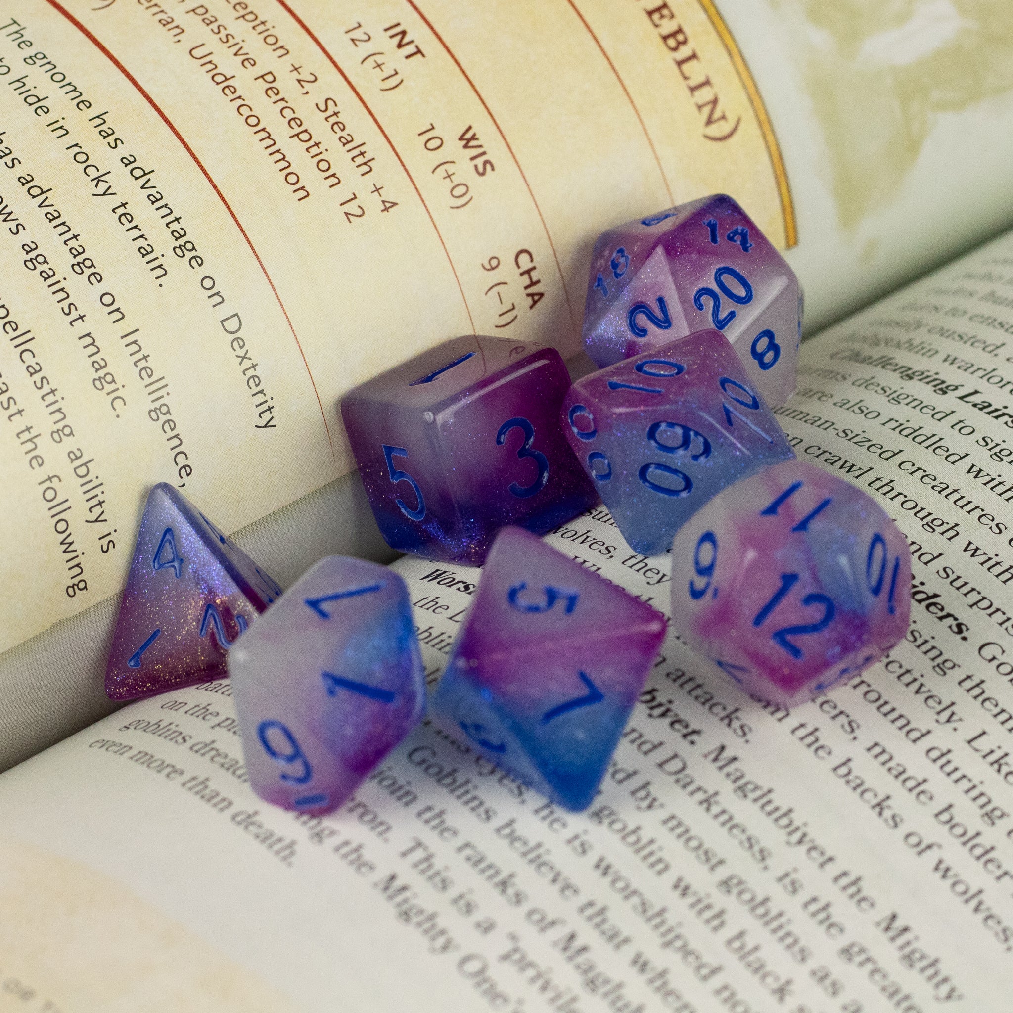 Emberlight Twilight Glow-in-the-Dark Dice Set - Purple and blue gradient seven-piece dice set with glow-in-the-dark numbers on open book pages.