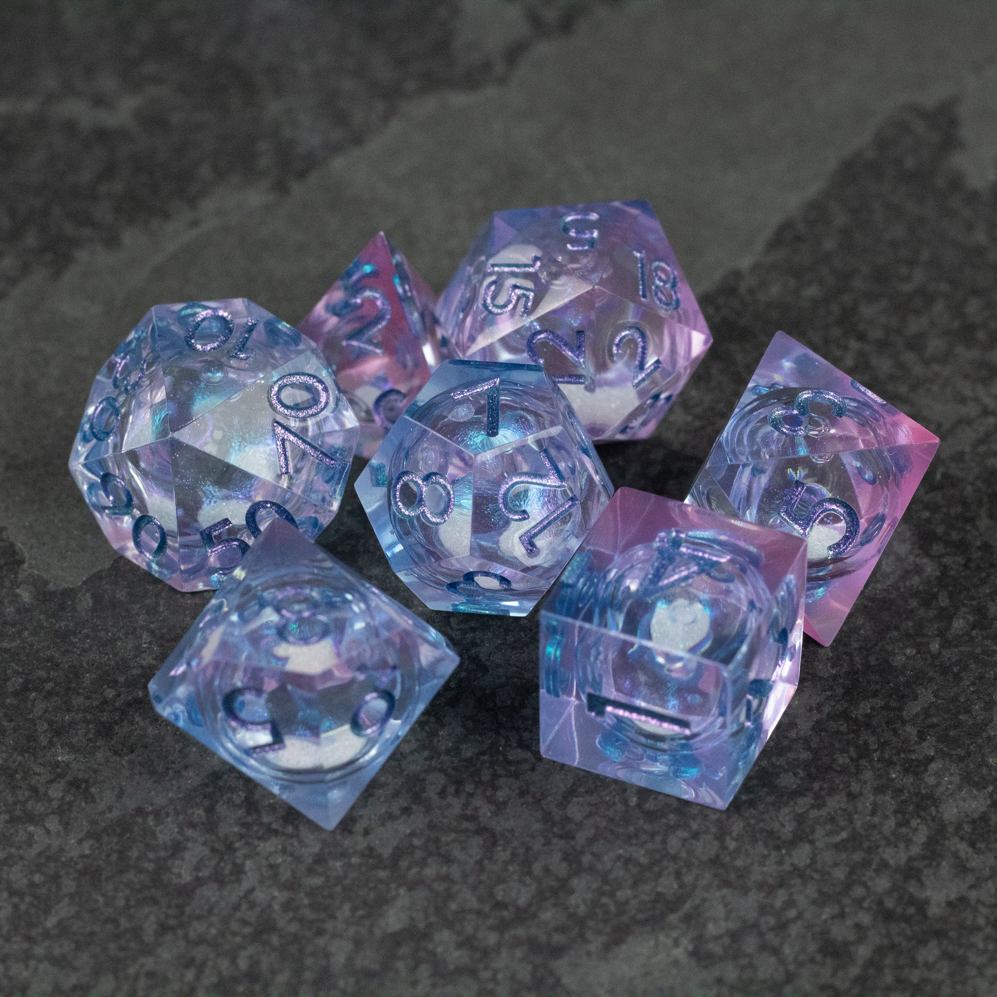 Fae Magic - Liquid Core Dice Set - Translucent blue and pink liquid core polyhedral dice set on dark surface.
