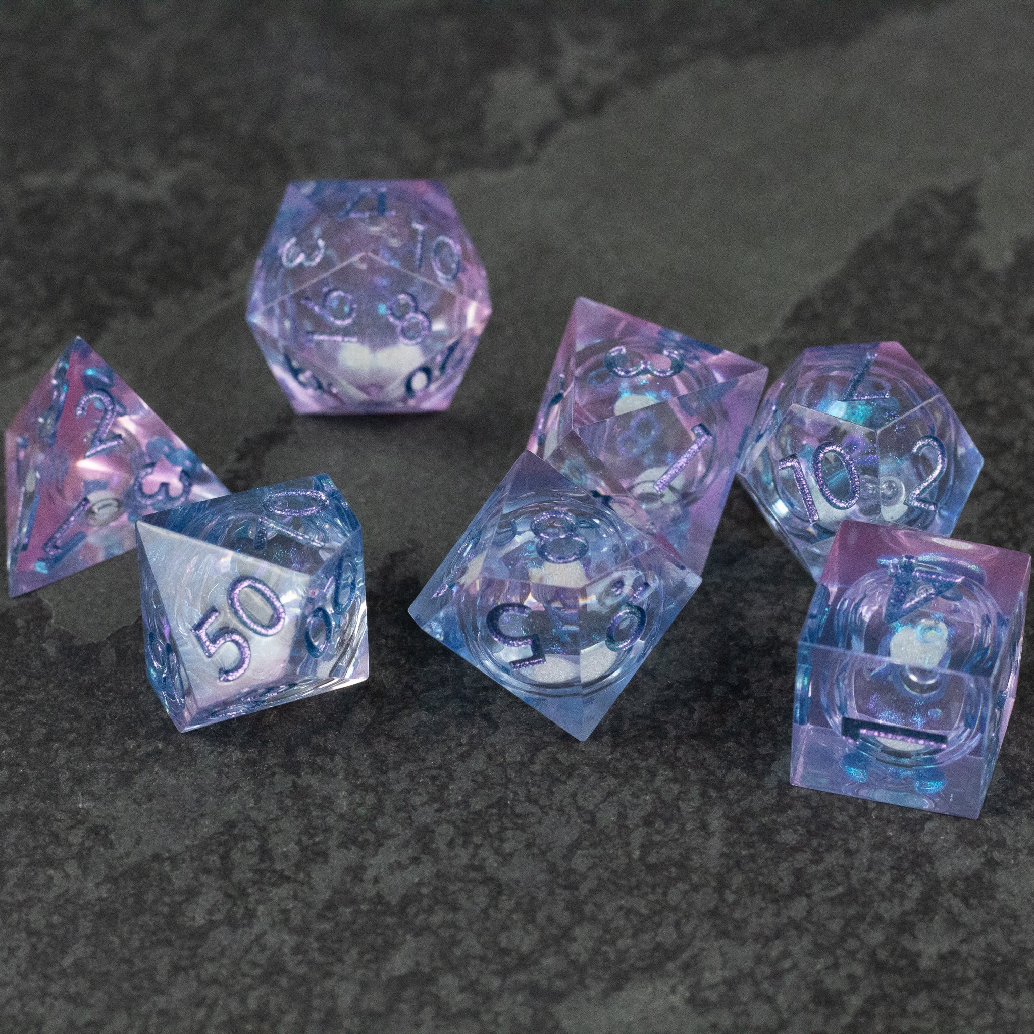 Fae Magic - Liquid Core Dice Set - Set of translucent pink and blue liquid core polyhedral dice with white numbers on dark textured background.