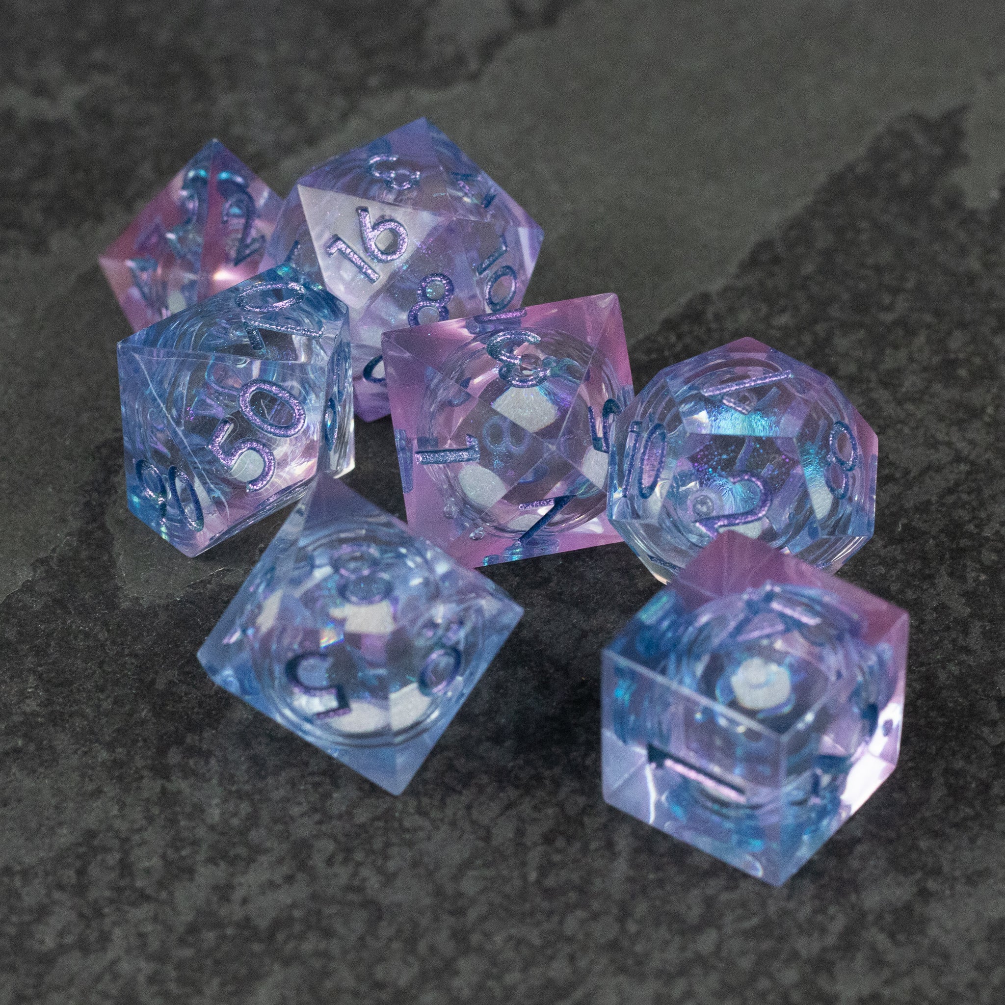 Fae Magic - Liquid Core Dice Set - Set of seven translucent polyhedral dice in swirling purple and blue hues with silver numbering.