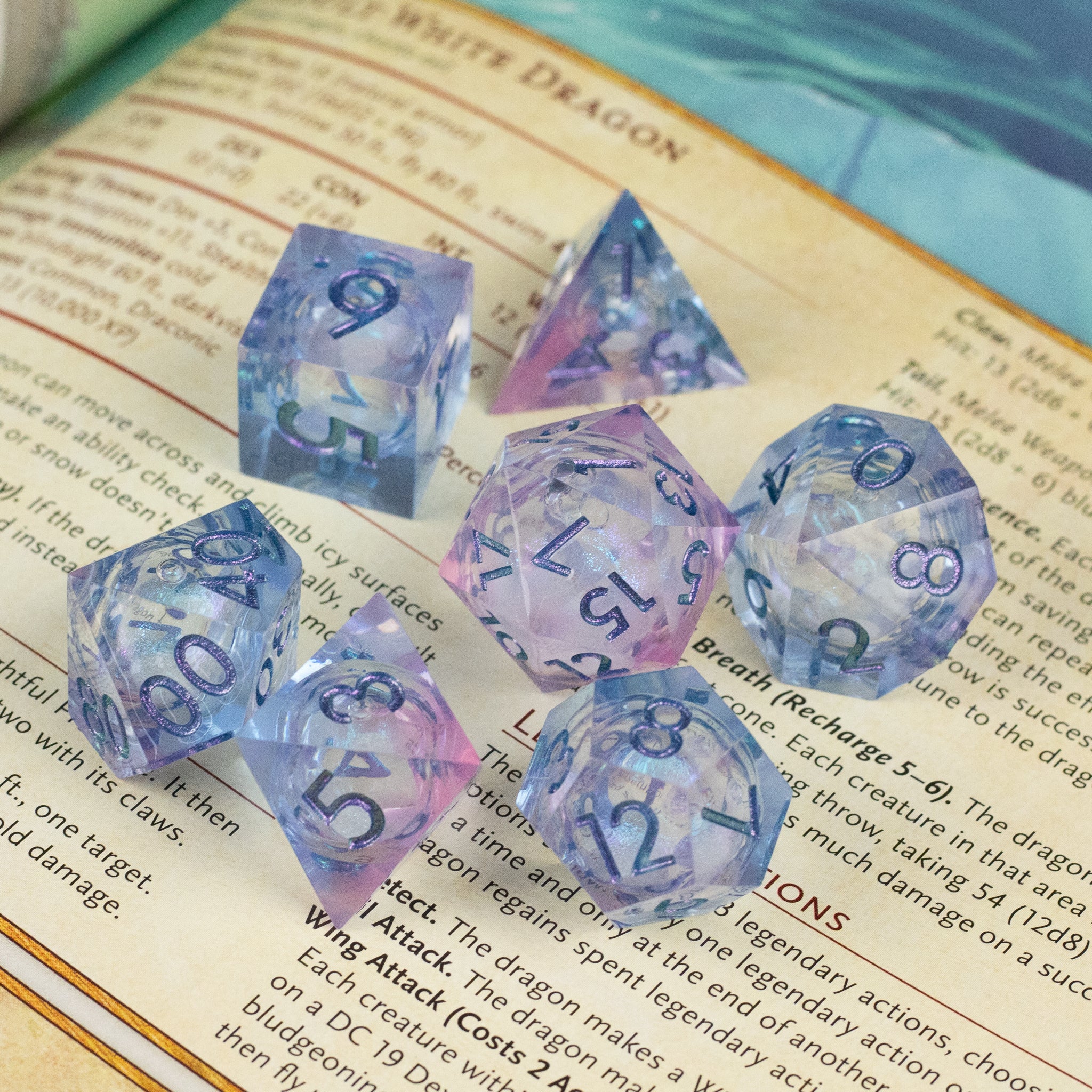 Fae Magic - Liquid Core Dice Set - Set of seven translucent polyhedral dice with swirling blue and pink liquid core, metallic blue numbers.