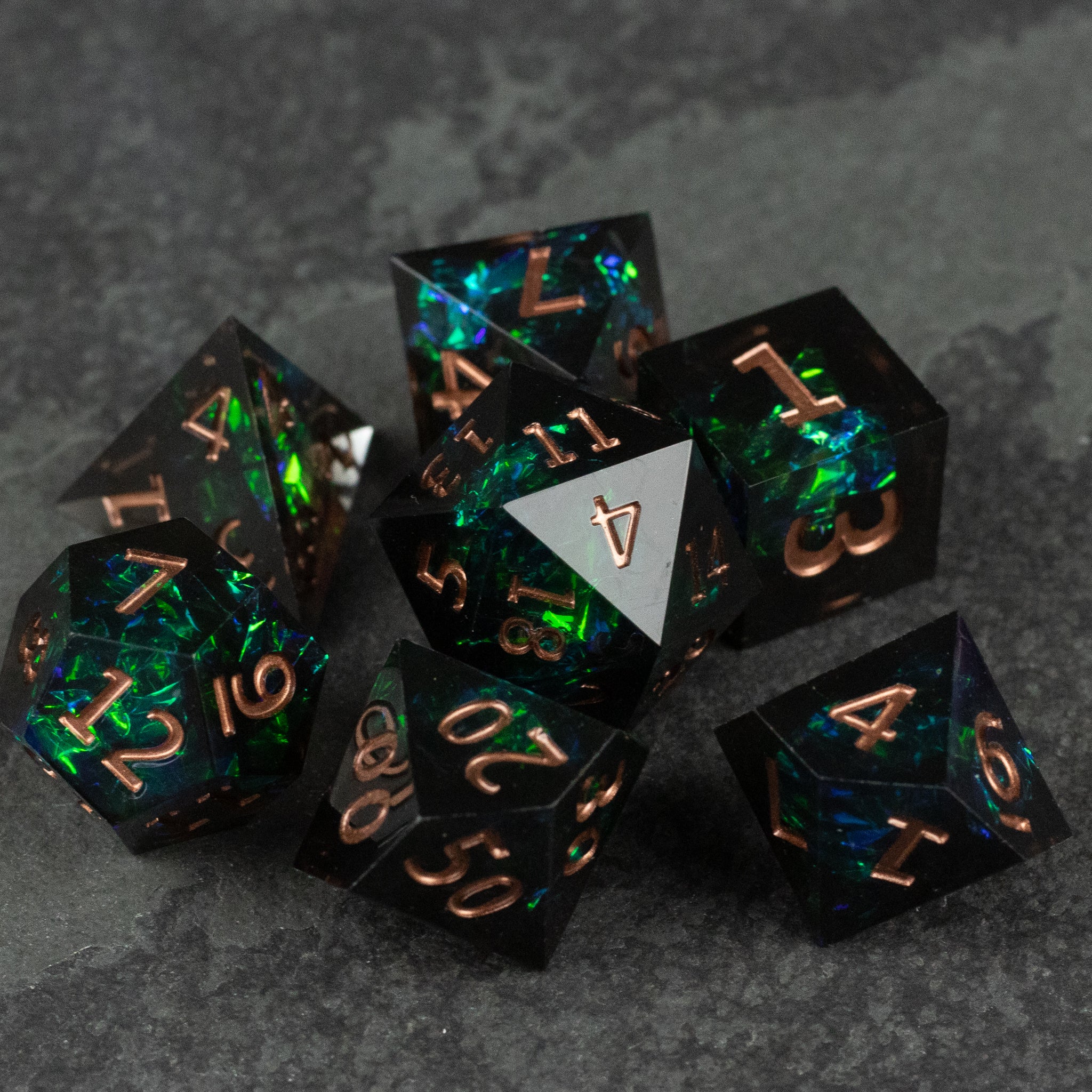 The Underdark Dice Set - Black sharp-edged dice with glowing green and blue iridescent highlights and copper numbers.