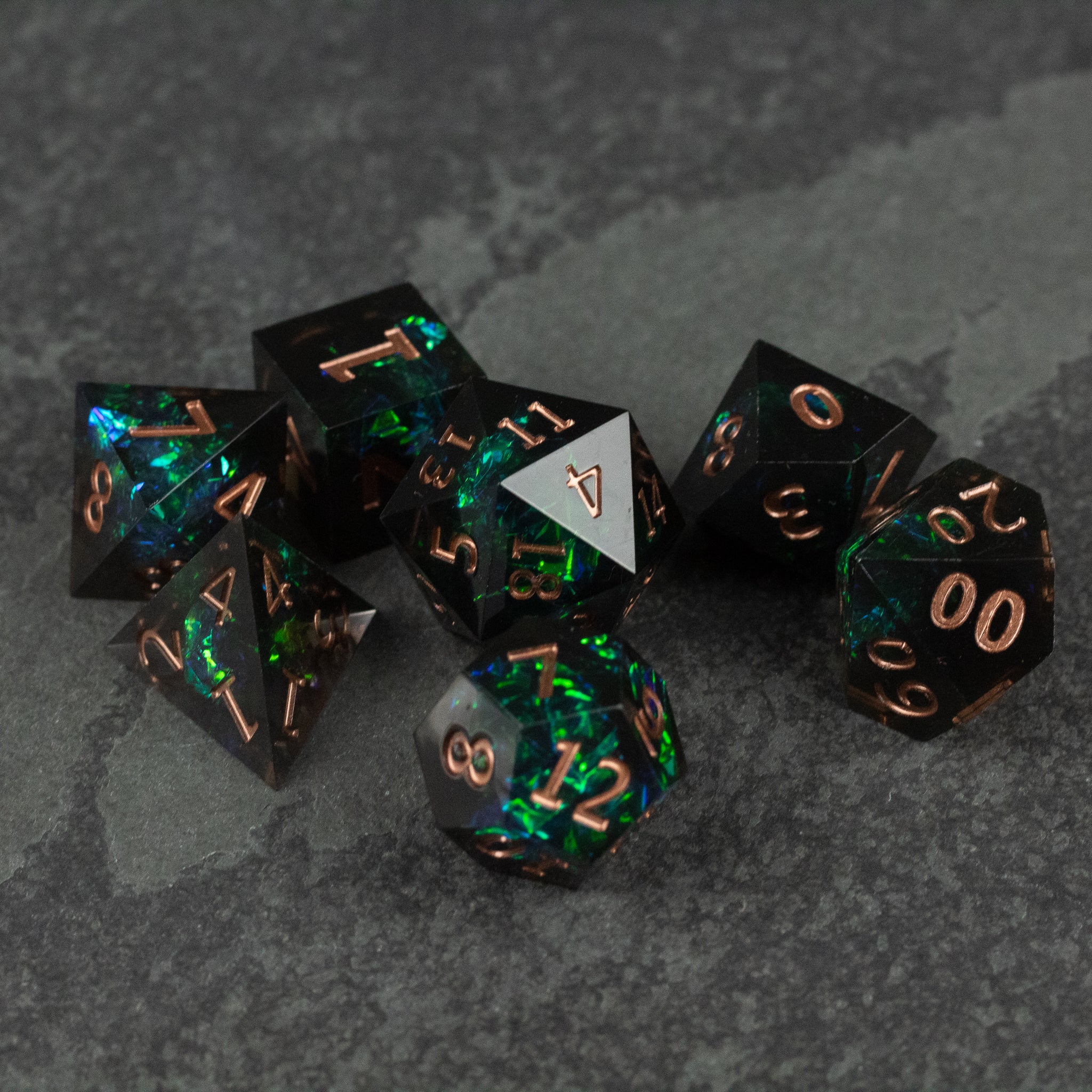 The Underdark Dice Set - Black and green marbled sharp-edged polyhedral dice set with copper numbers on dark stone background.