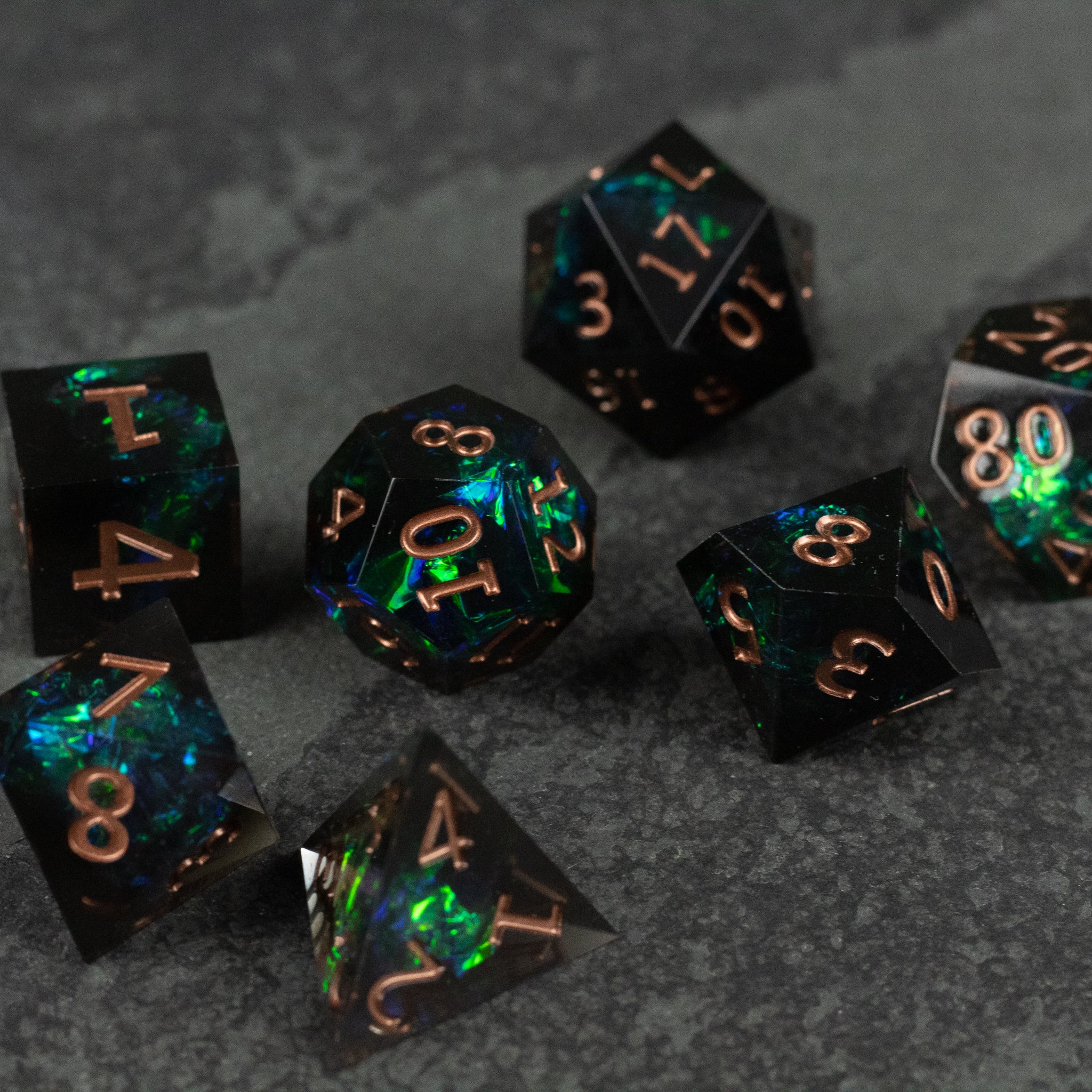 The Underdark Dice Set - Black sharp-edged dice set with glowing green and blue swirls and copper numbers on gray surface.