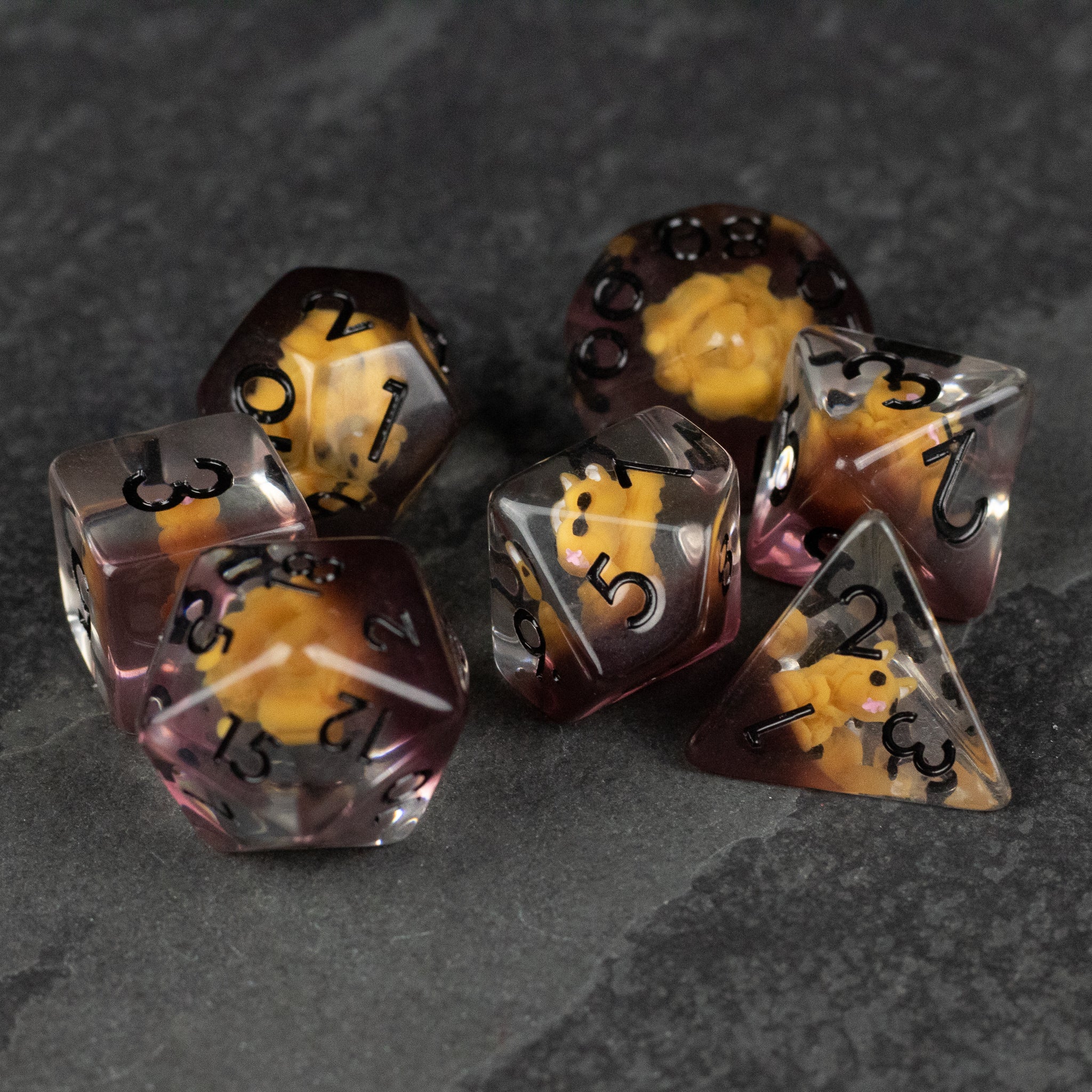 Squirrel Dice Set - Set of seven polyhedral dice with transparent black and amber swirls, black numbers, and a resin material on dark stone.