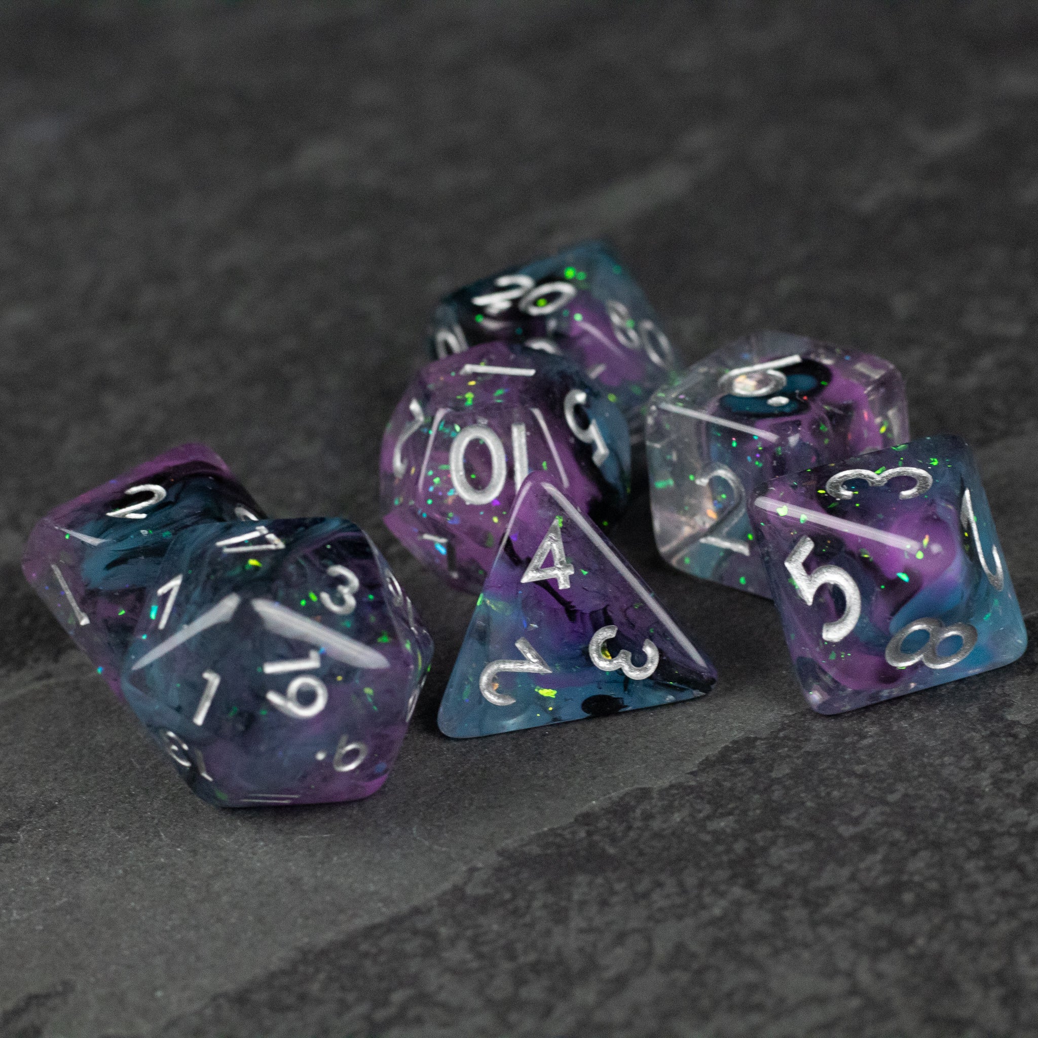 Purple and Black Spellweaver Dice Set - Seven purple and black translucent polyhedral dice with white numbering on a dark textured surface.