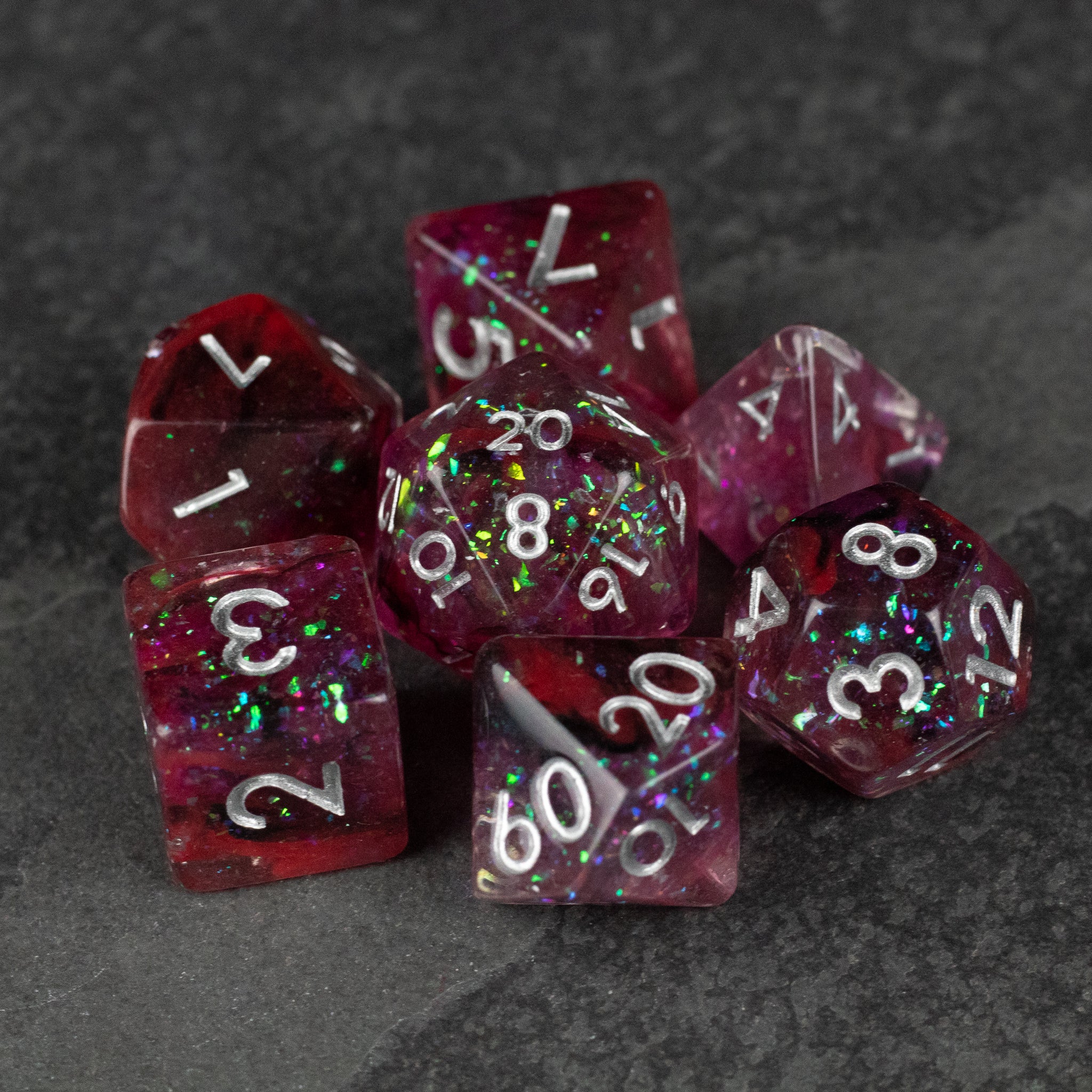Black and red Spellweaver Dice Set - Set of seven translucent black and red polyhedral dice with white numbers and multicolored glitter specks.