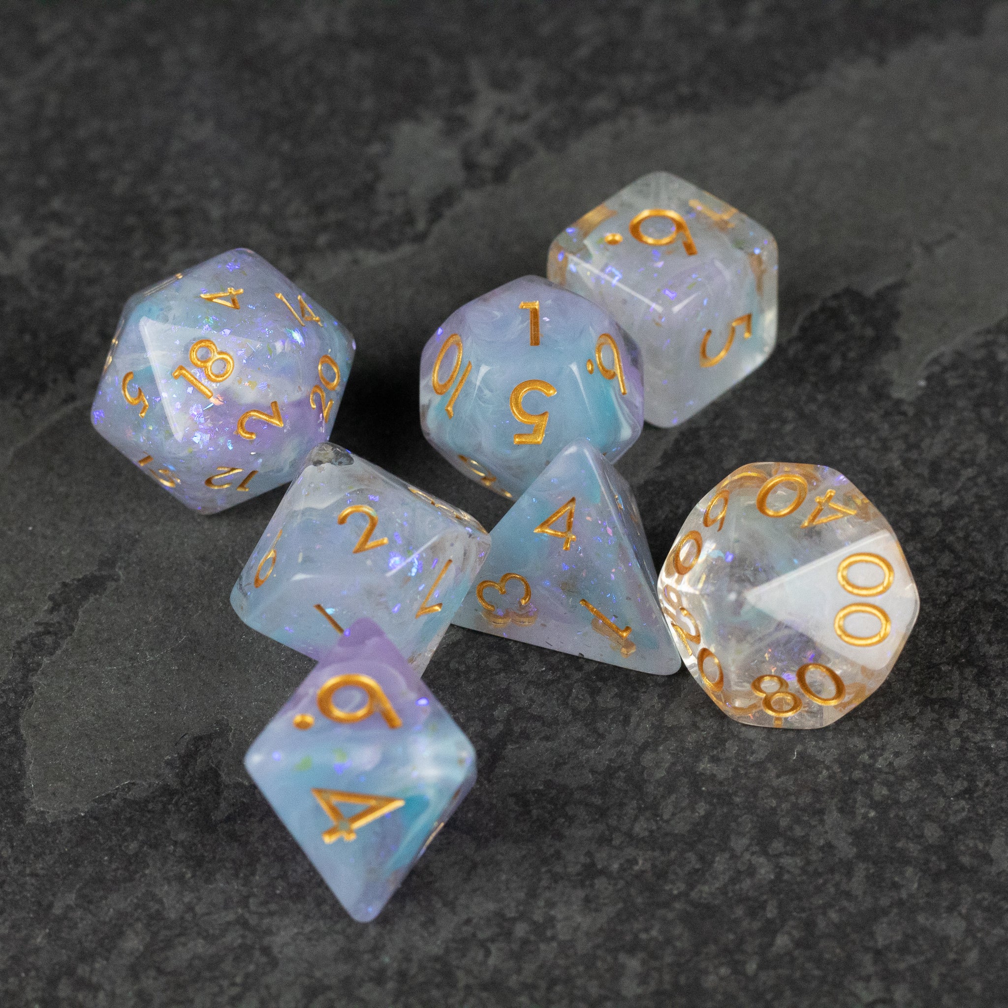 Spellbound Dice Set - Seven translucent polyhedral dice with purple and gold swirls and gold numbers on a dark stone surface.