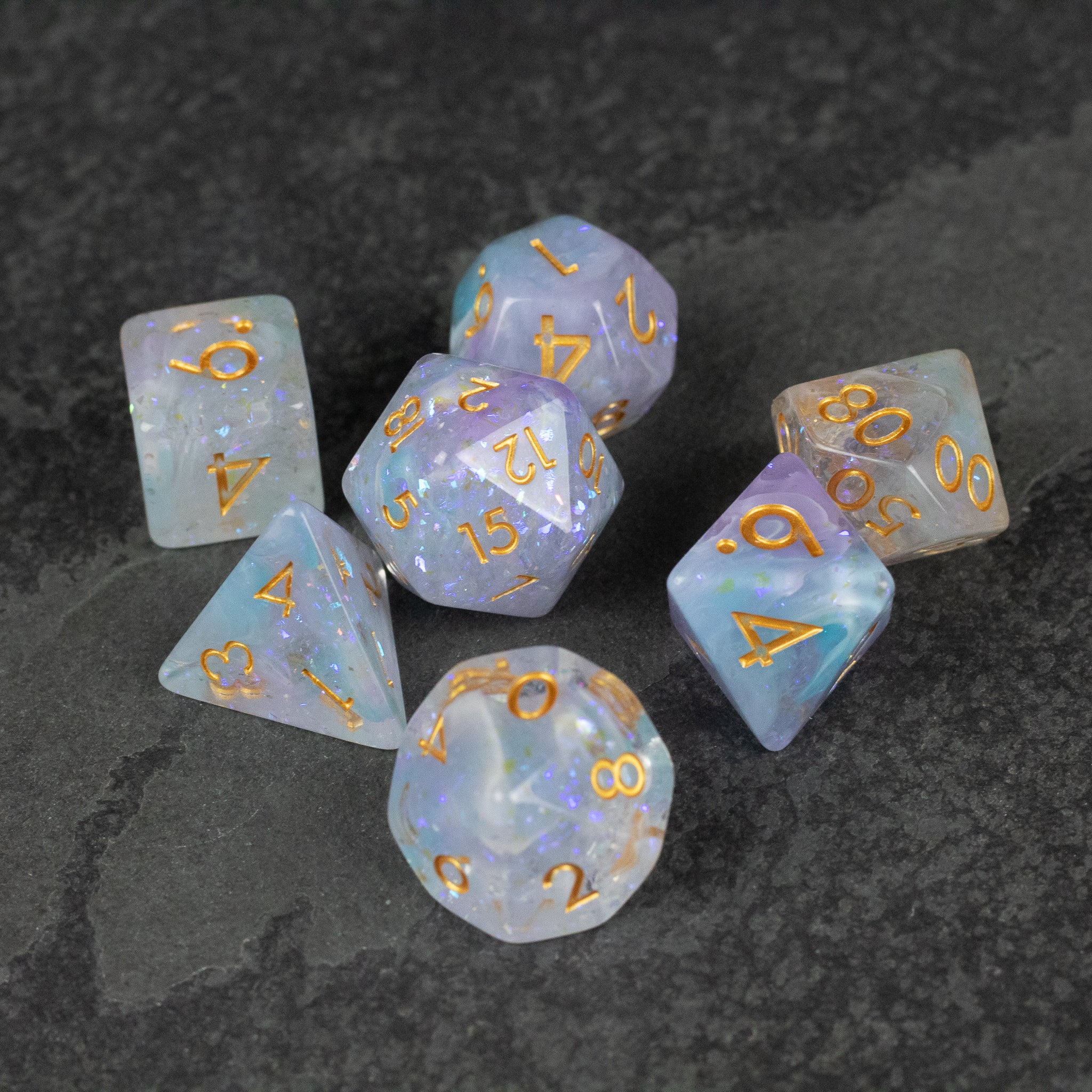 Spellbound Dice Set - Translucent blue and white polyhedral dice set with gold numbers on a dark stone surface.
