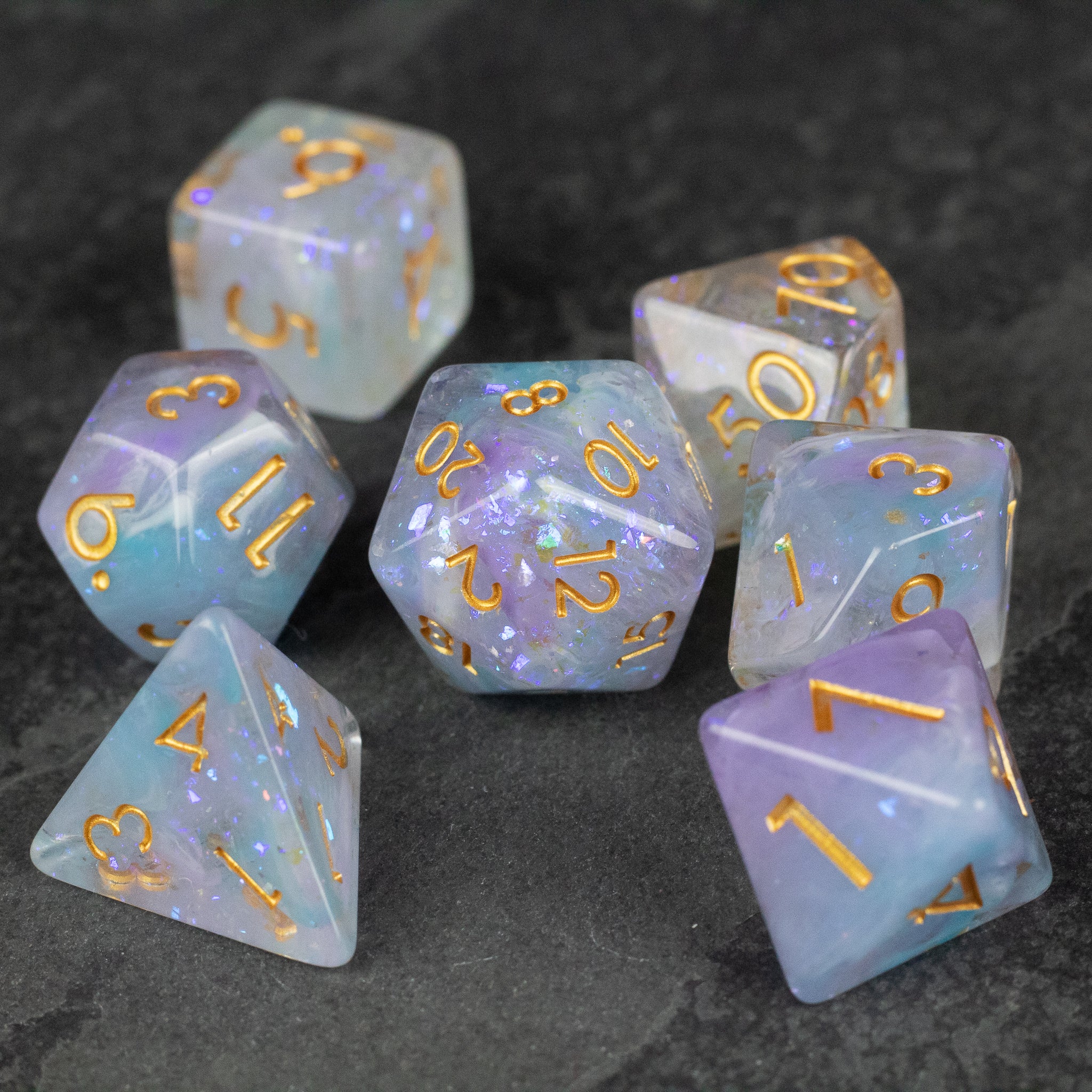 Spellbound Dice Set - Translucent spellbound dice set with a mix of lavender and blue hues, gold numbering, and glitter accents.