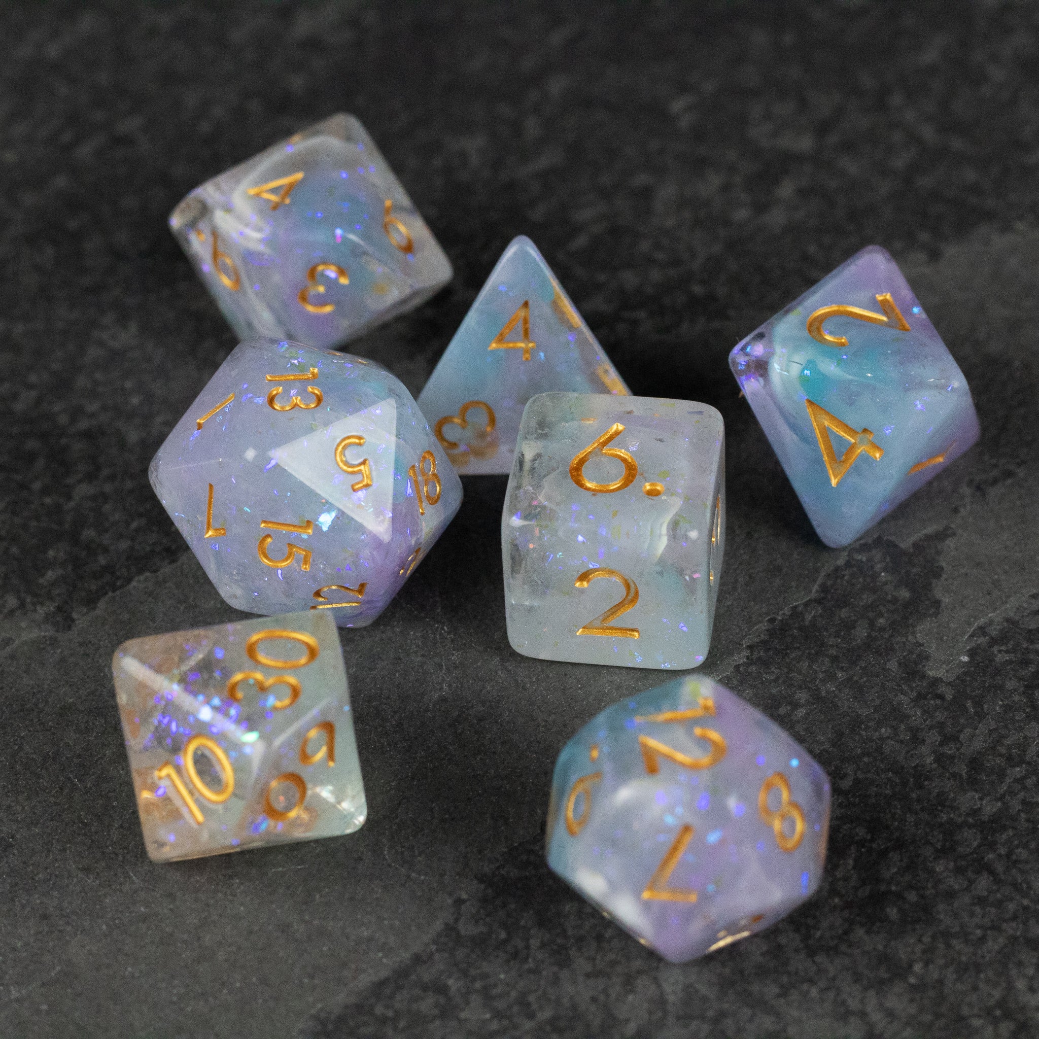 Spellbound Dice Set - Seven translucent polyhedral dice with swirling purple and gold flecks, featuring gold numbers.