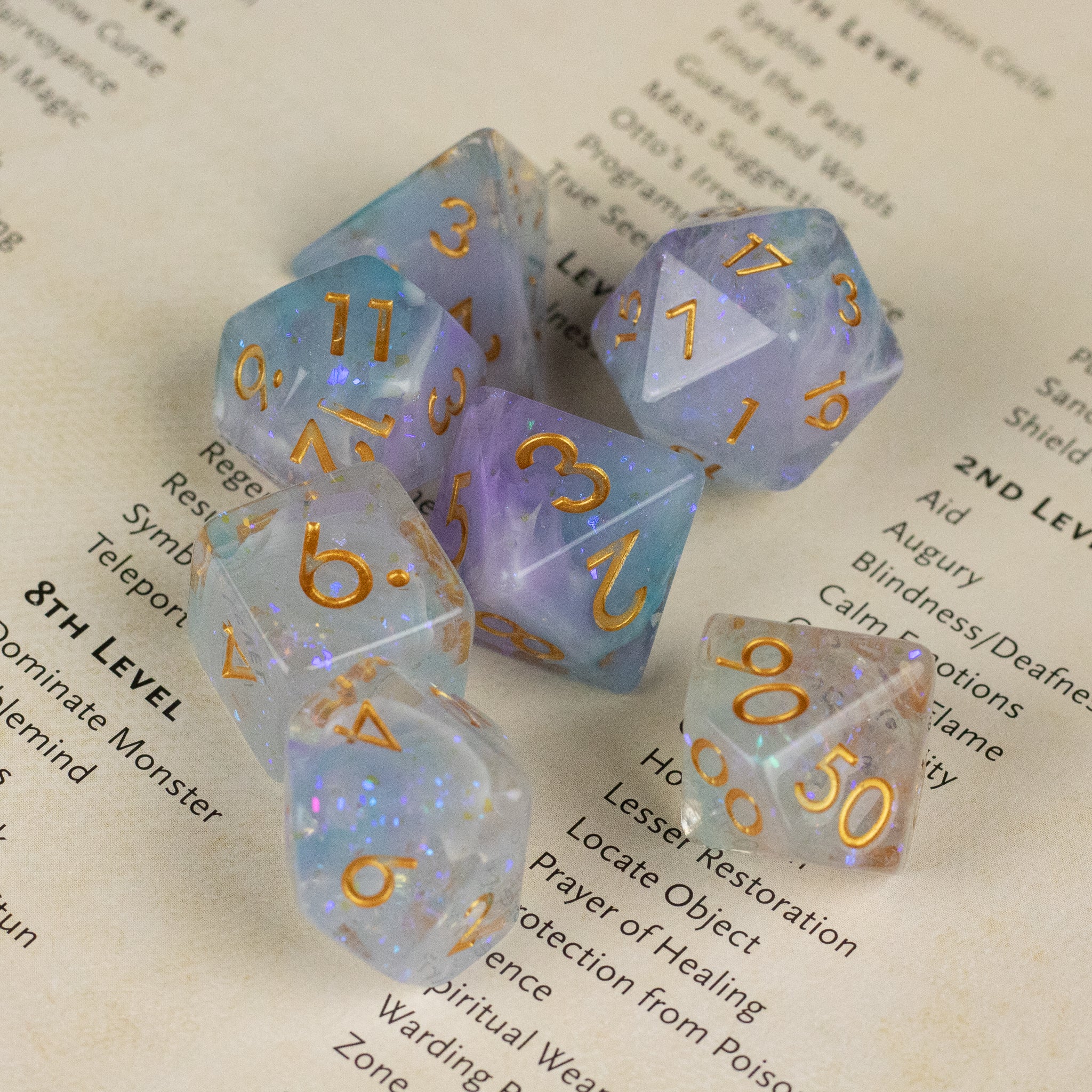 Spellbound Dice Set - Set of translucent purple and blue polyhedral dice with gold numbers, featuring a shimmering, speckled finish.
