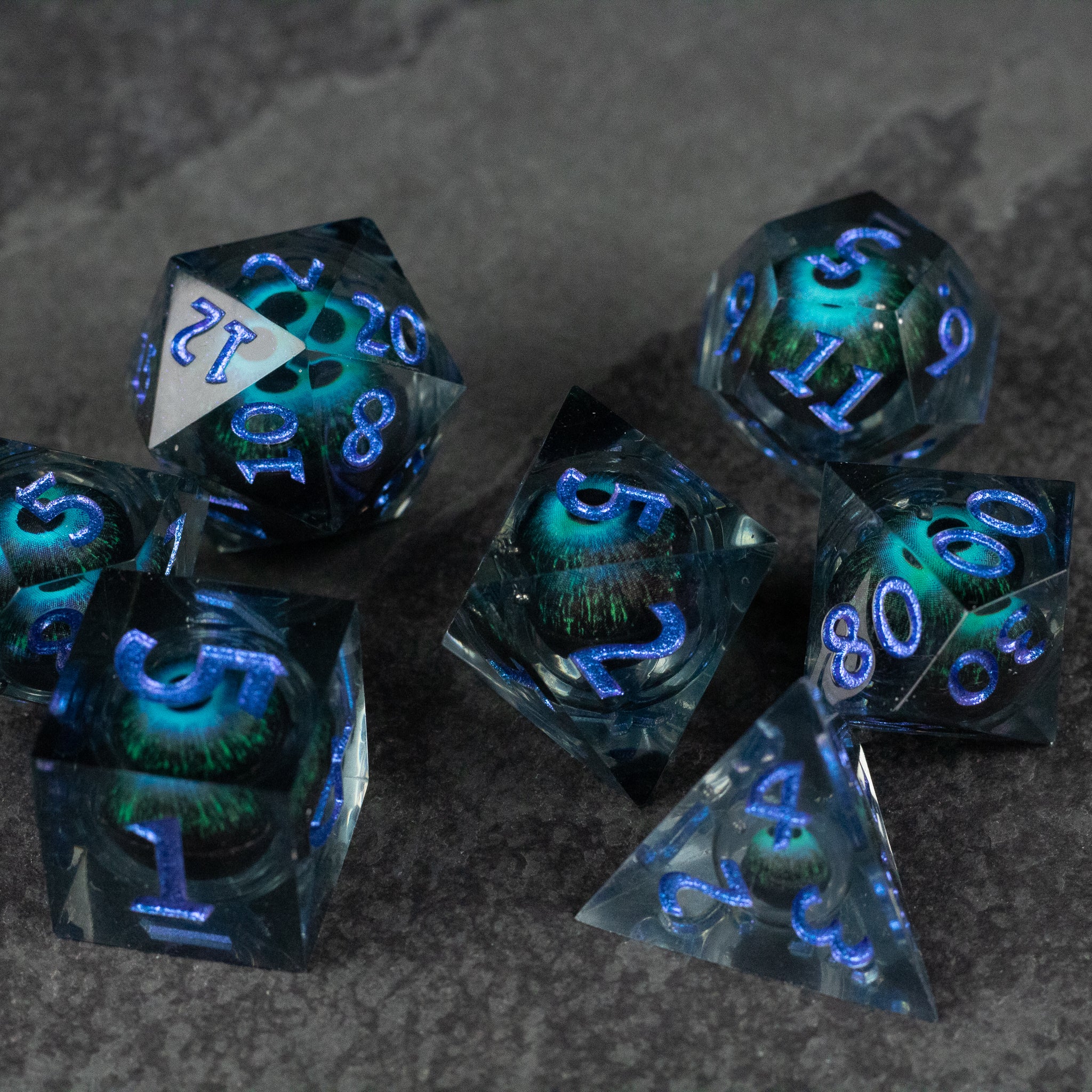 Blue Beholder's Eye Dice Set - Seven blue translucent polyhedral dice with glowing liquid core and sharp edges, featuring light blue numbers.