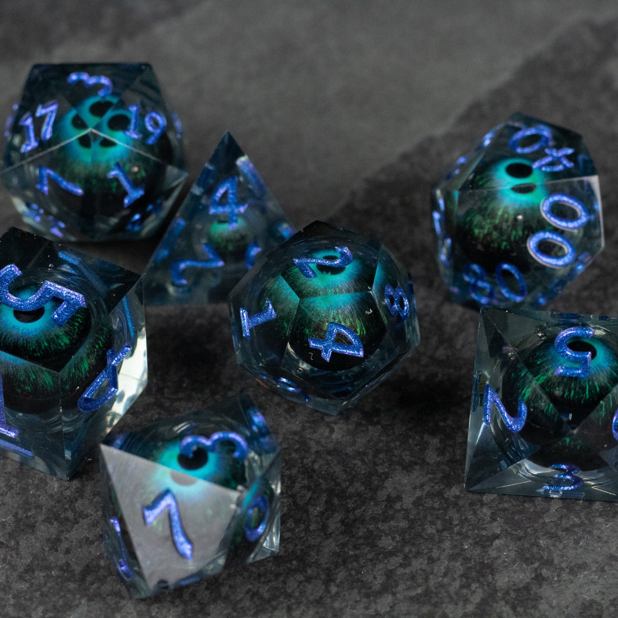 Blue Beholder's Eye Dice Set - Blue and green translucent polyhedral dice set with glowing sharp-edged numerals and liquid core effect.