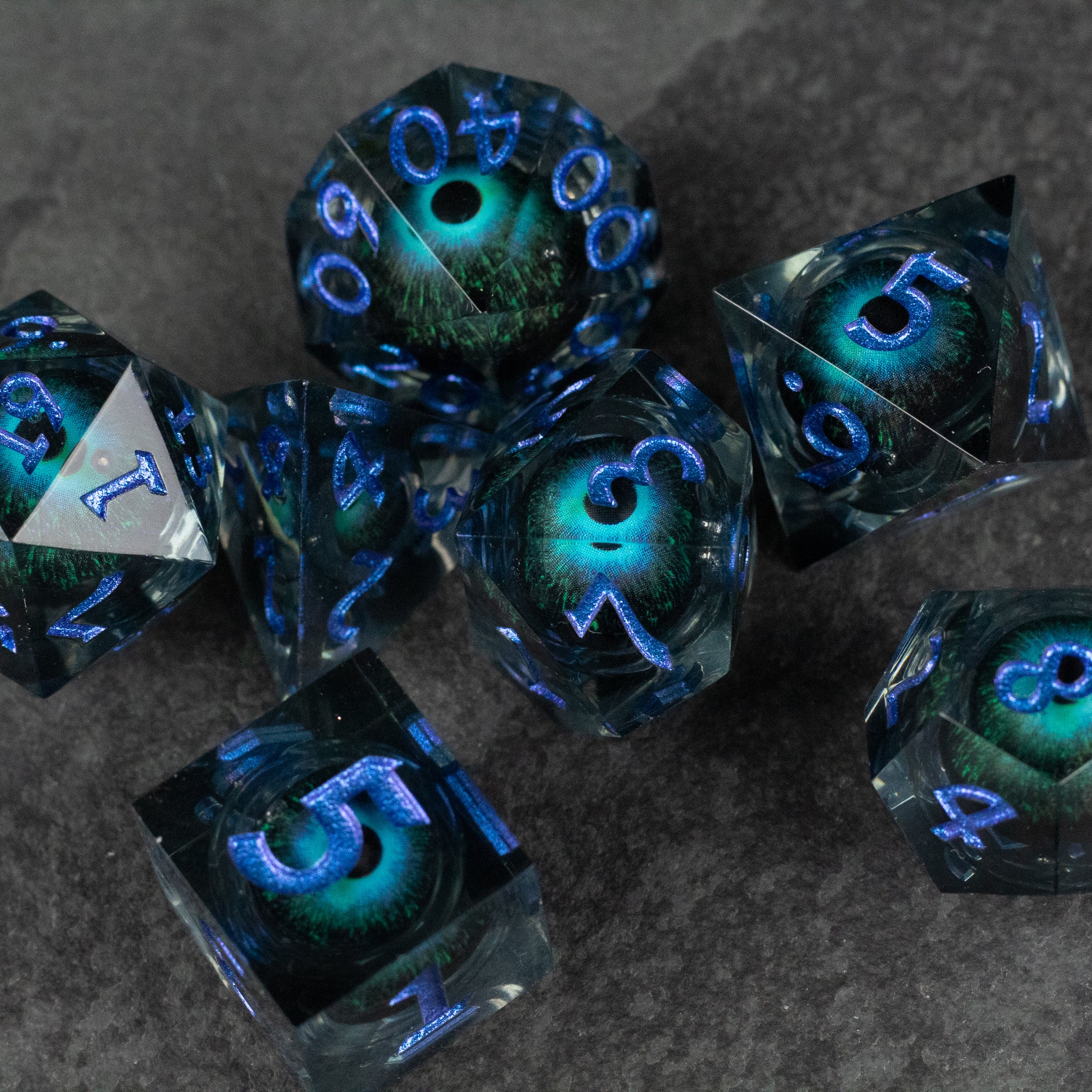 Blue Beholder's Eye Dice Set - Dark blue polyhedral dice set with glowing green eyes and sharp blue numbers.