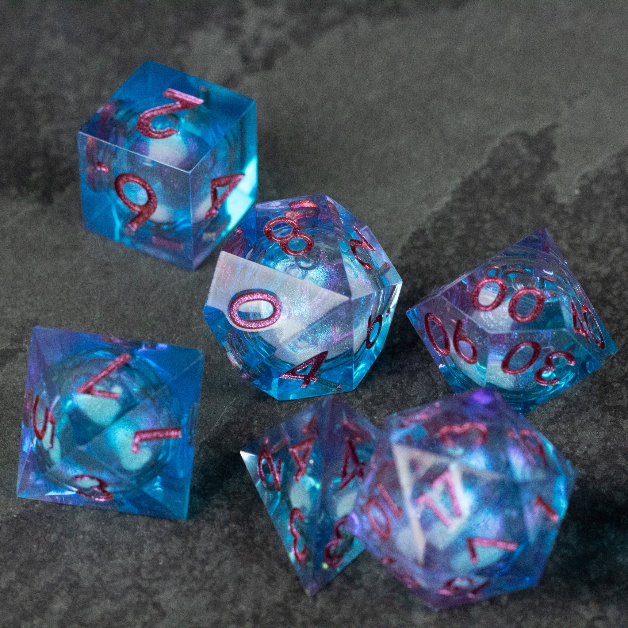 Crystallomancy Dice Set - Translucent blue sharp-edge polyhedral dice with red numbering and swirling liquid core inside.