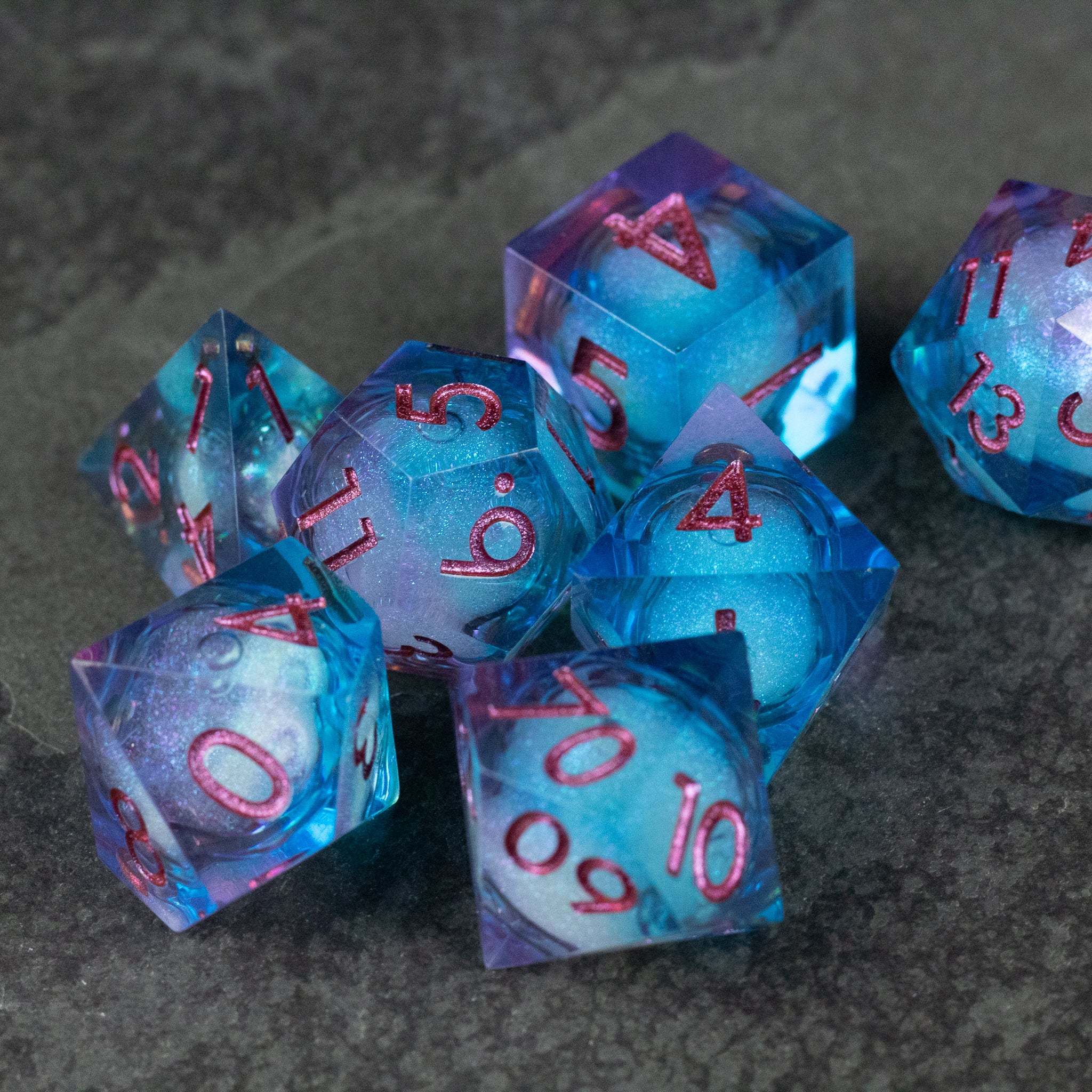 Crystallomancy Dice Set - Set of blue translucent sharp-edged dice with red numbers and liquid core design on dark surface.