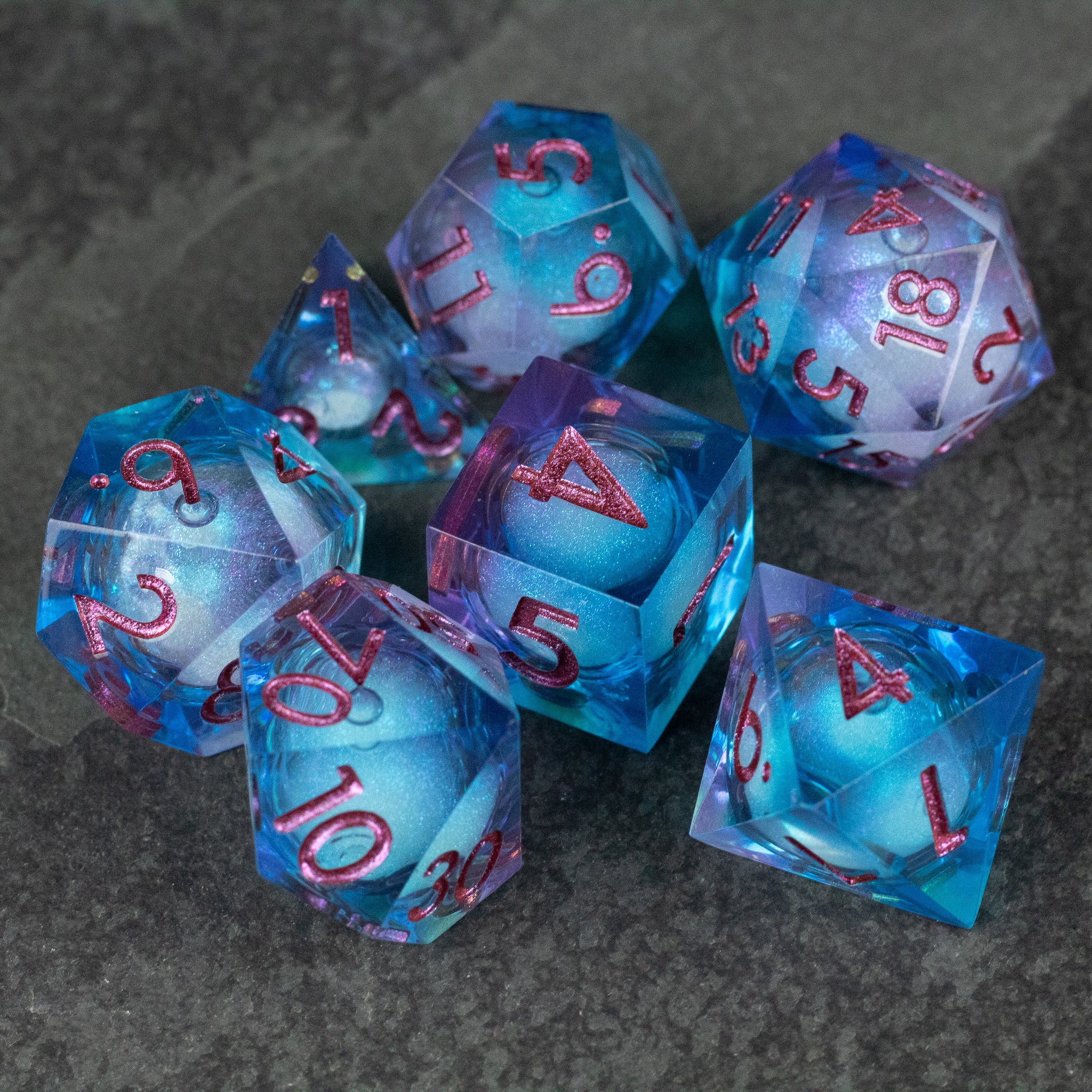 Crystallomancy Dice Set - Set of seven sharp-edged polyhedral dice with liquid core in blue and purple hues, red numbering.