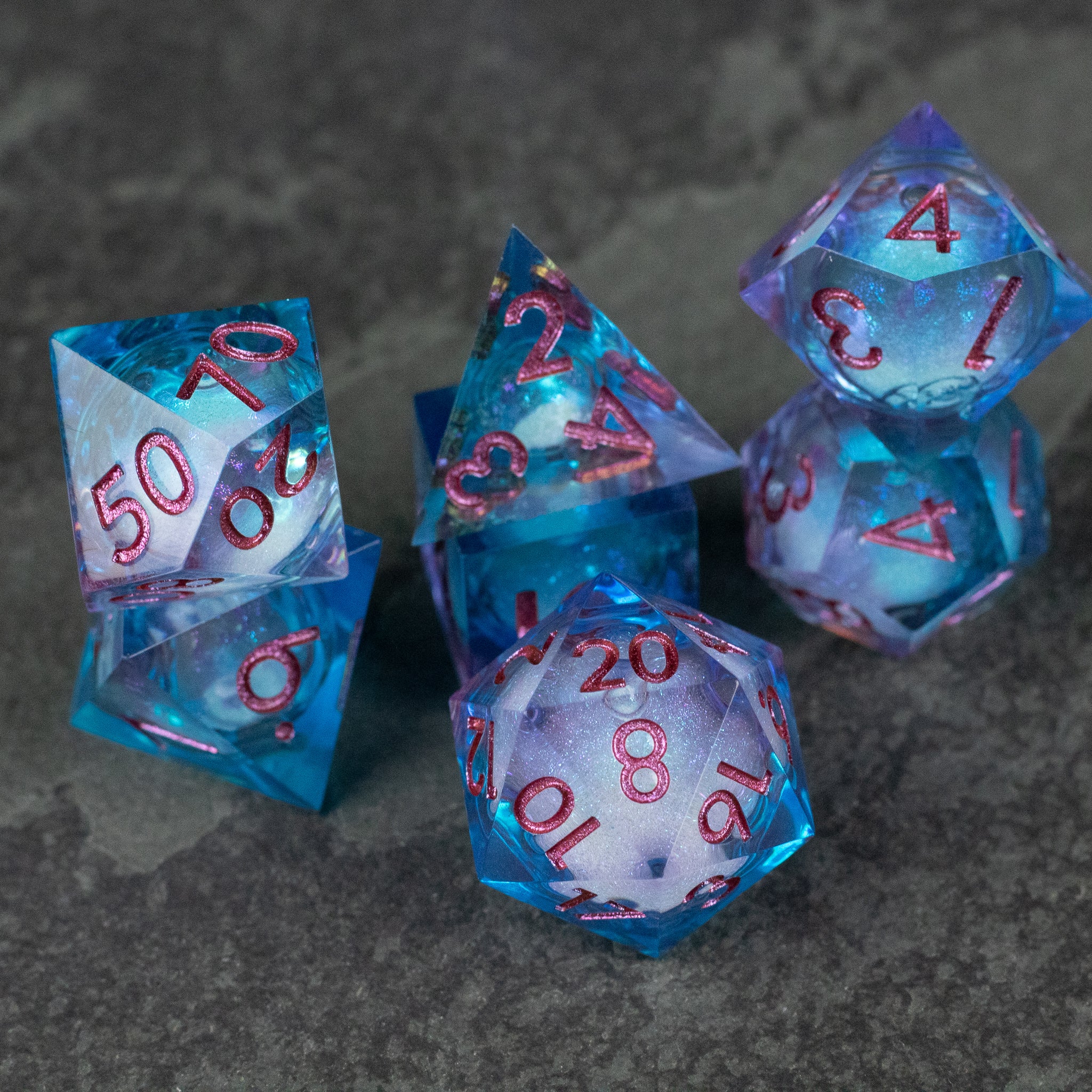 Crystallomancy Dice Set - Seven translucent blue polyhedral dice with sharp edges and red numerals, featuring a liquid core design.