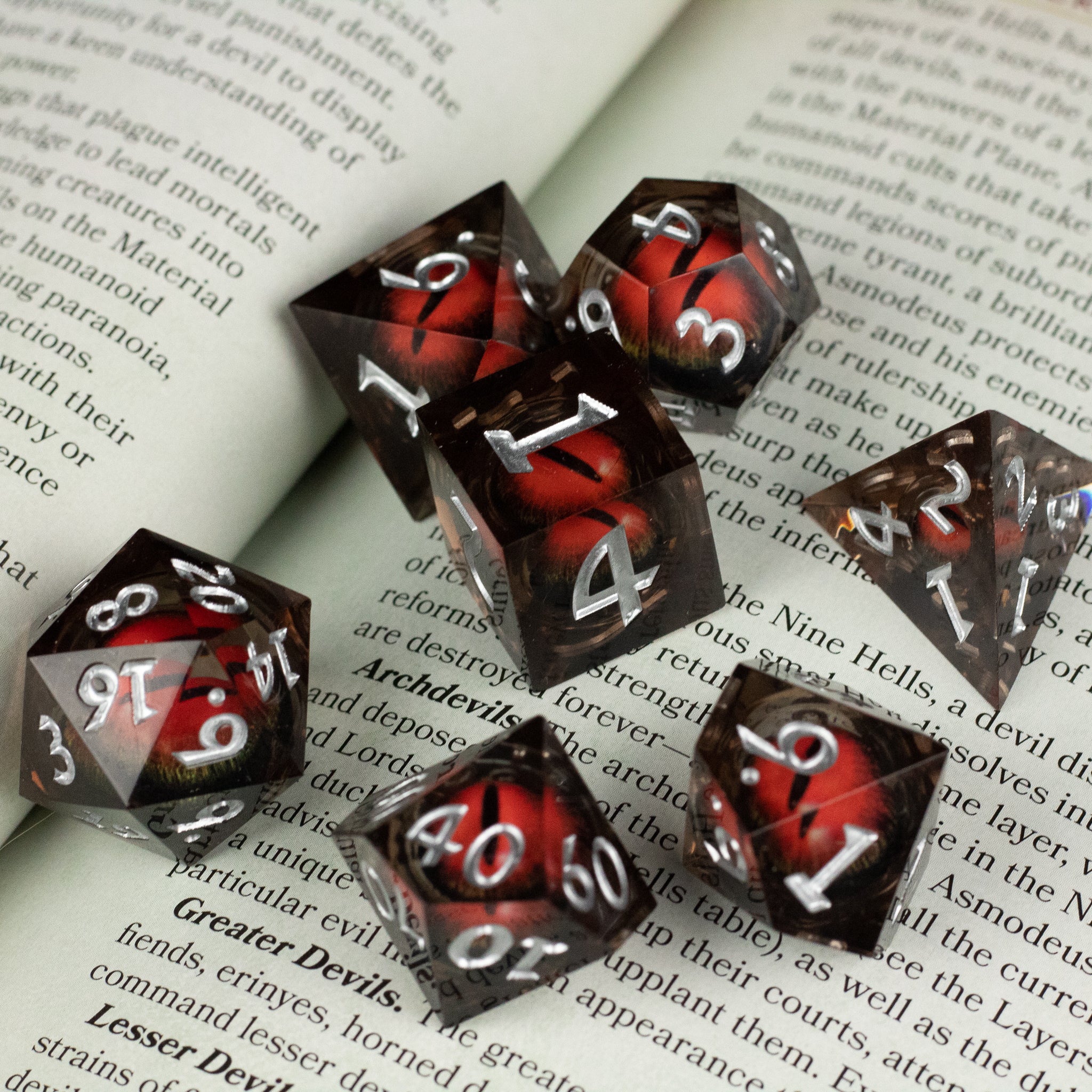 Orange Beholder's Eye Dice Set - Seven orange and black marbled sharp-edged polyhedral dice with white numbering scattered on an open book.