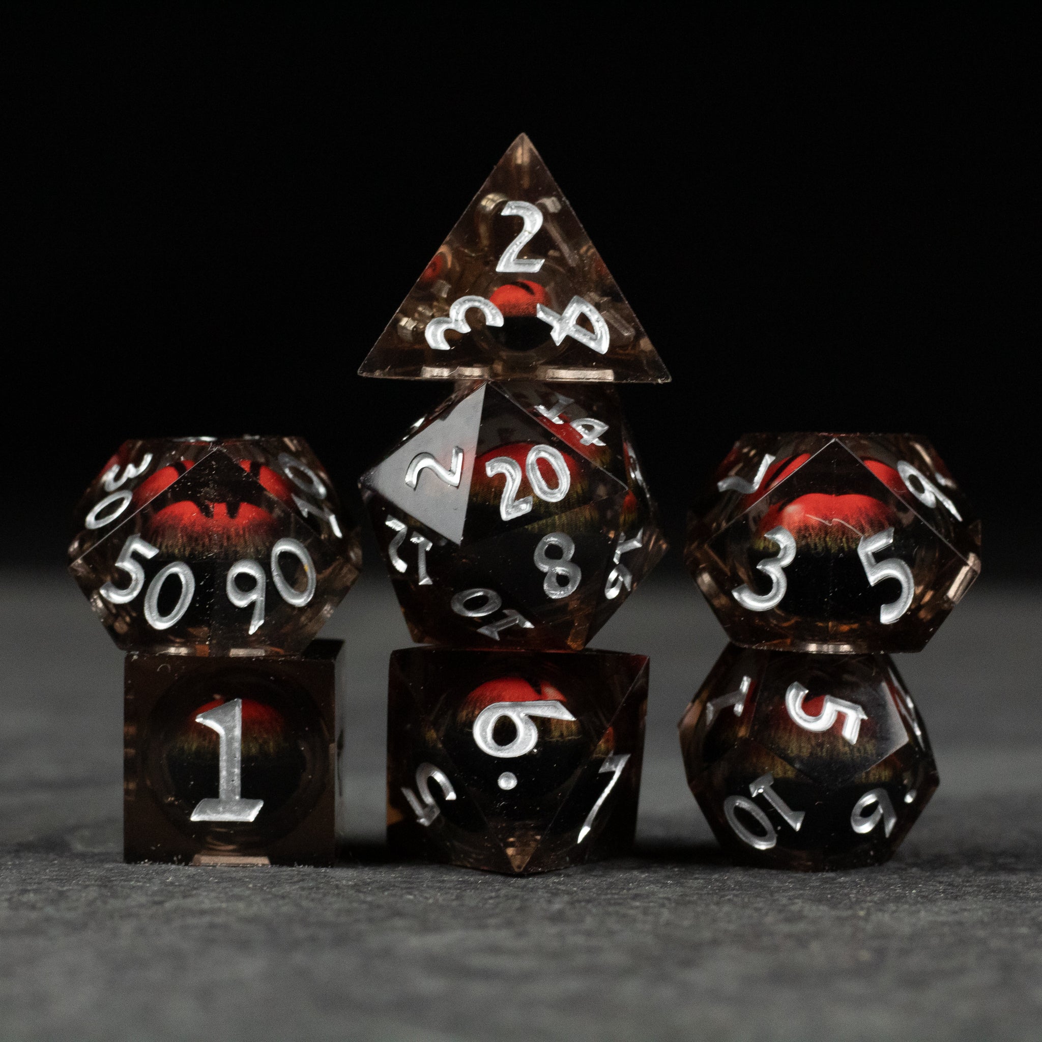 Orange Beholder's Eye Dice Set - Sharp-edged translucent black dice with swirling orange liquid core and white numbers, including d20 and d6 shapes.