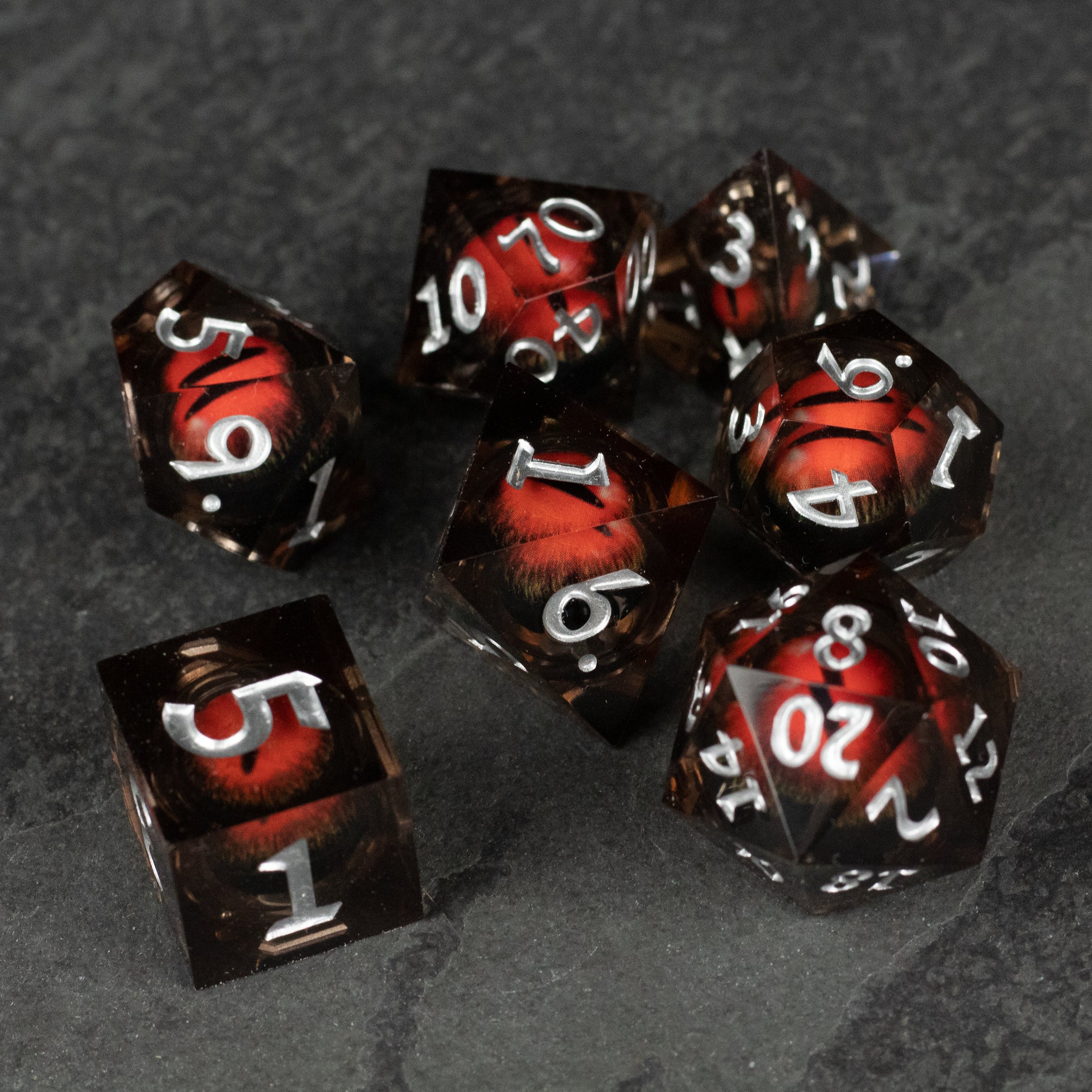 Orange Beholder's Eye Dice Set - Seven black dice with sharp edges featuring swirling orange liquid core and white numbers on gray surface.