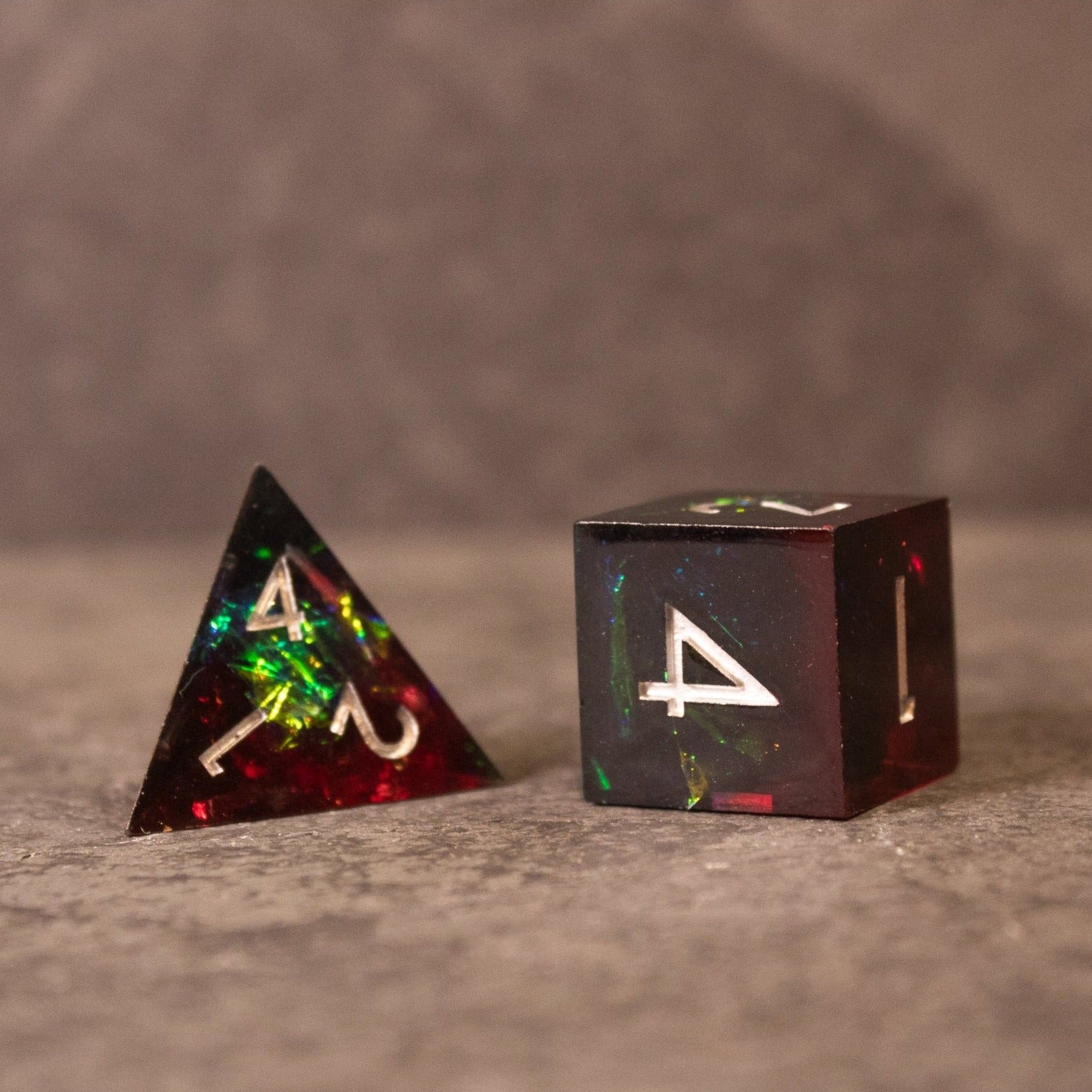 Blood Magic - Sharp Edge Opalescent Dice - Black sharp-edged tetrahedron and cube dice with opalescent red and green flecks, white numbering.