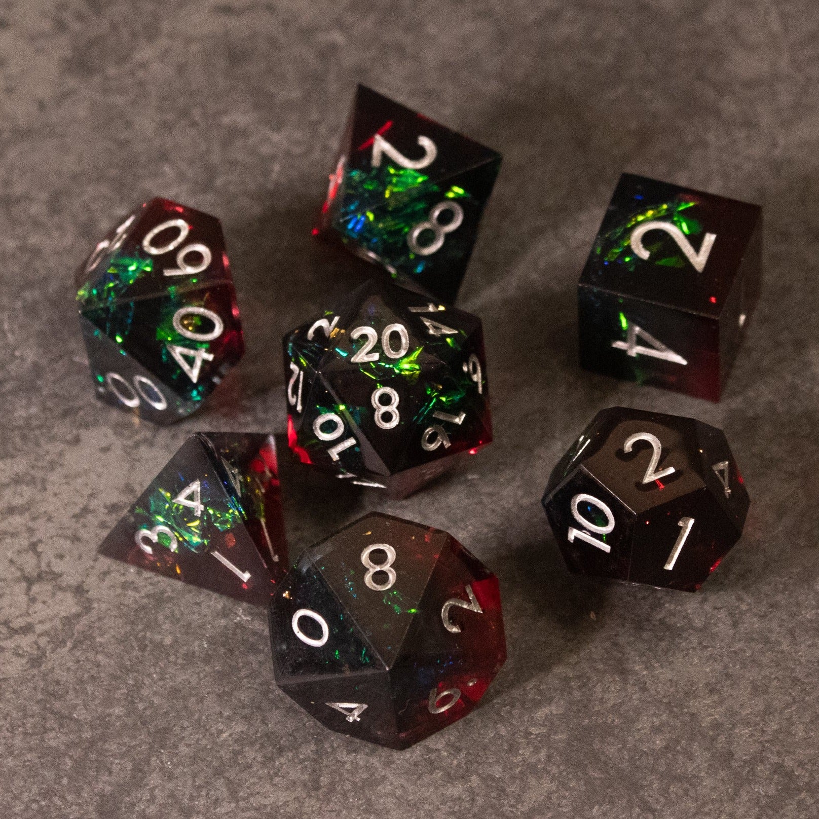 Blood Magic - Sharp Edge Opalescent Dice - Set of seven sharp-edged polyhedral dice with opalescent green, red, and black swirls, white numbering.