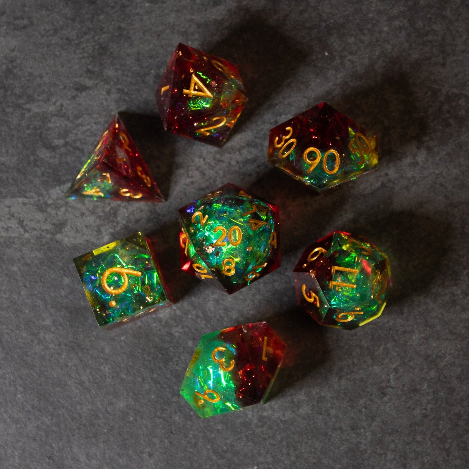 Fairy Fire - Sharp Edge Opalescent Dice - Seven sharp-edge dice with a fiery blend of red, green, and gold opalescent colors and gold numbering.