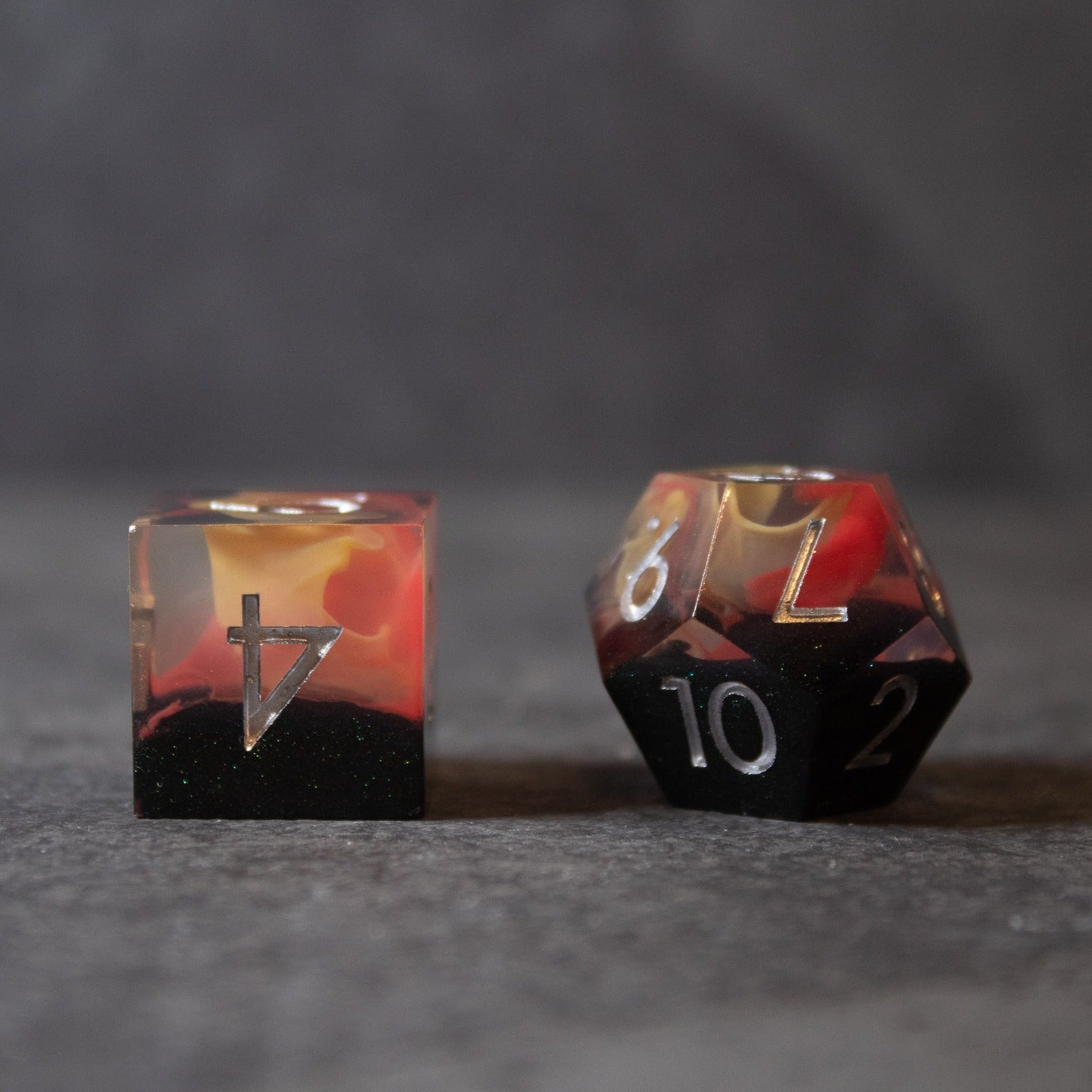 Widowgast's Flame - Sharp Edge Dice - Two sharp-edged translucent dice with fiery red, orange, and black swirls, featuring white numbers.