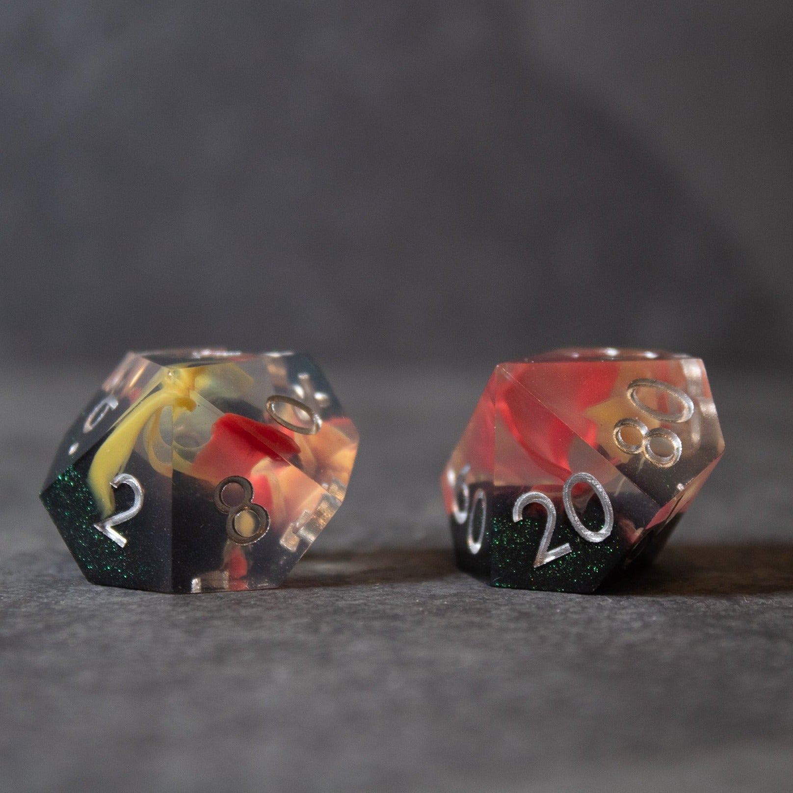 Widowgast's Flame - Sharp Edge Dice - Two sharp-edged polyhedral dice with red, black, and gold flame-like swirl patterns and white numbers on a dark surface.
