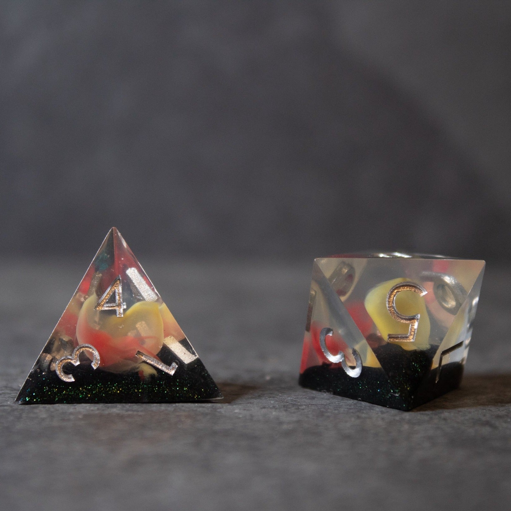 Widowgast's Flame - Sharp Edge Dice - Transparent sharp-edged polyhedral dice with red and yellow swirling flames and black speckled bases.