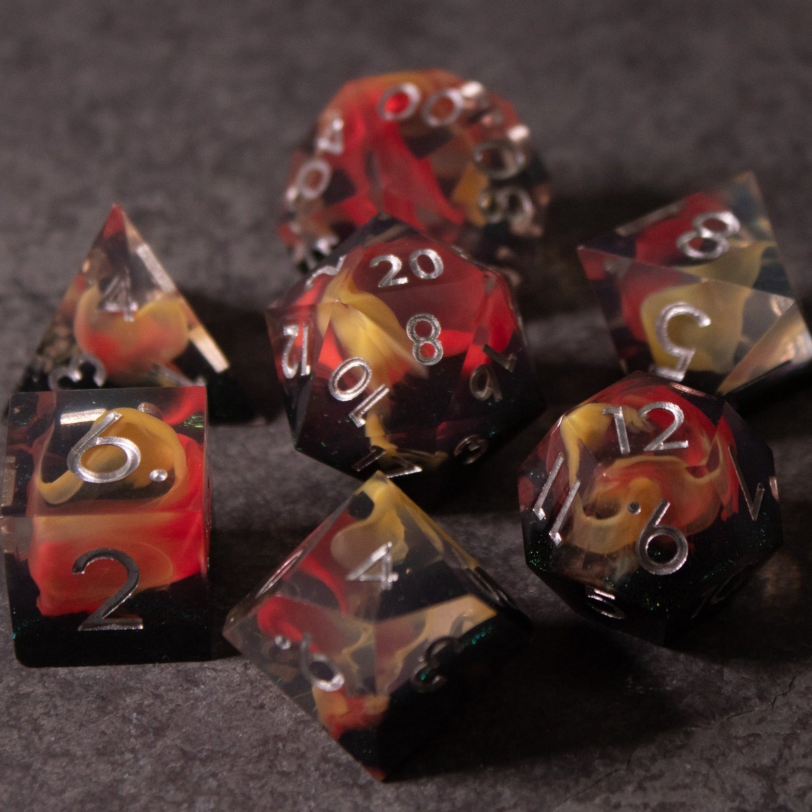 Widowgast's Flame - Sharp Edge Dice - Set of seven sharp-edged polyhedral dice in black, red, and yellow swirl with white numbering.