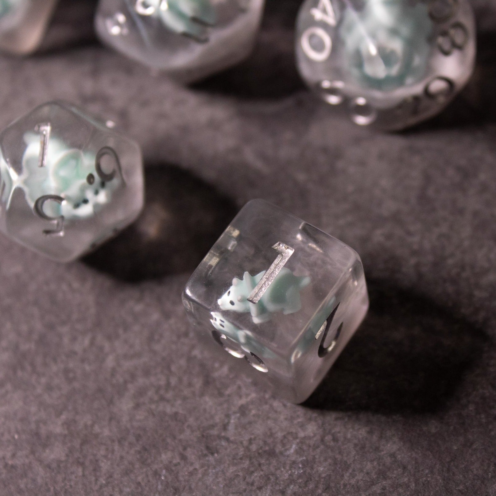 Dinosaur Dice Set - Triceratops - Translucent clear dice with tiny teal Triceratops figures inside and black number markings on a dark surface.