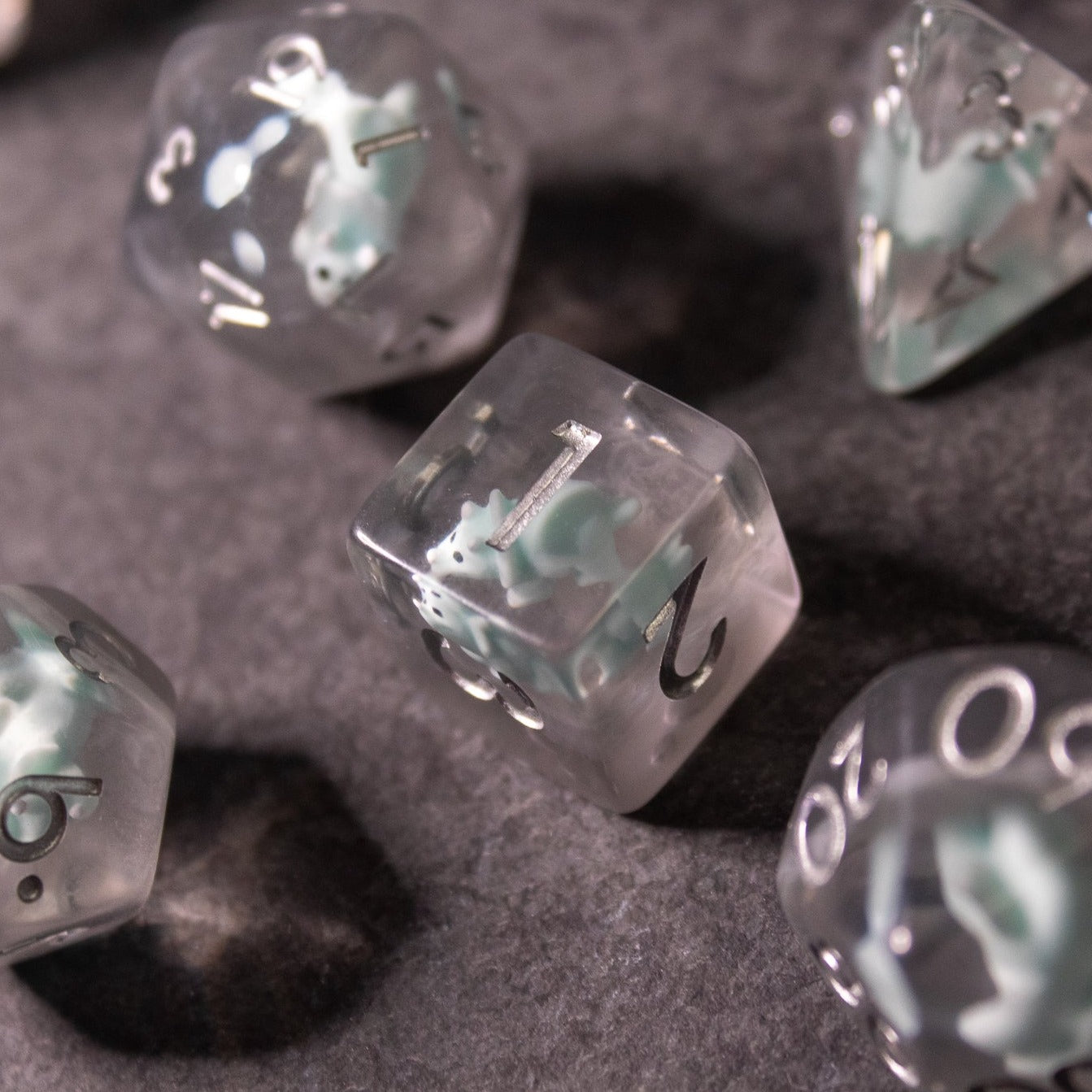 Dinosaur Dice Set - Triceratops - Clear polyhedral dice with embedded small green Triceratops dinosaur figures and white numbering.