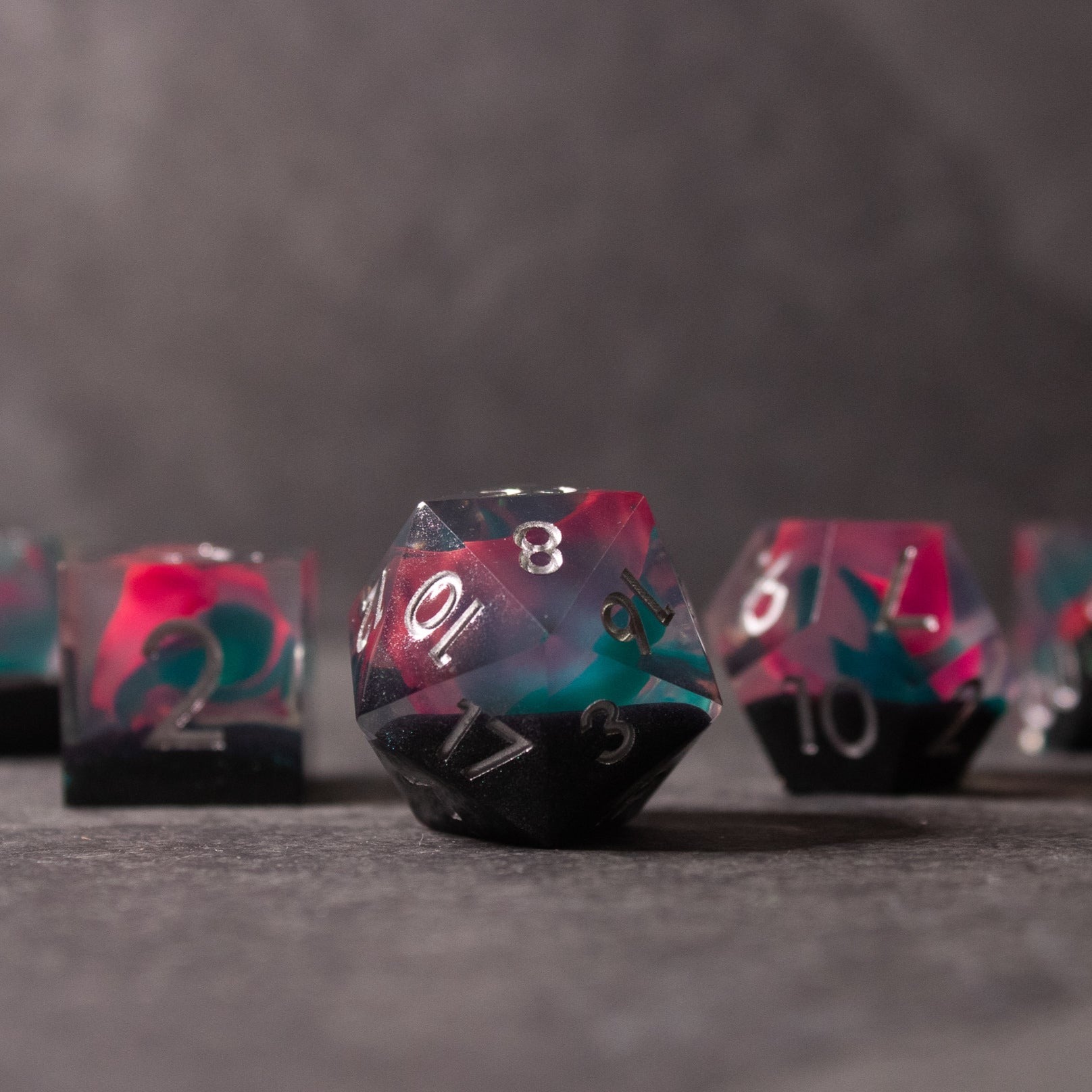 Pink & Green Flame Sharp Edge Dice Set - Set of sharp-edged dice with pink and green swirl colors and white numbering on a dark surface.