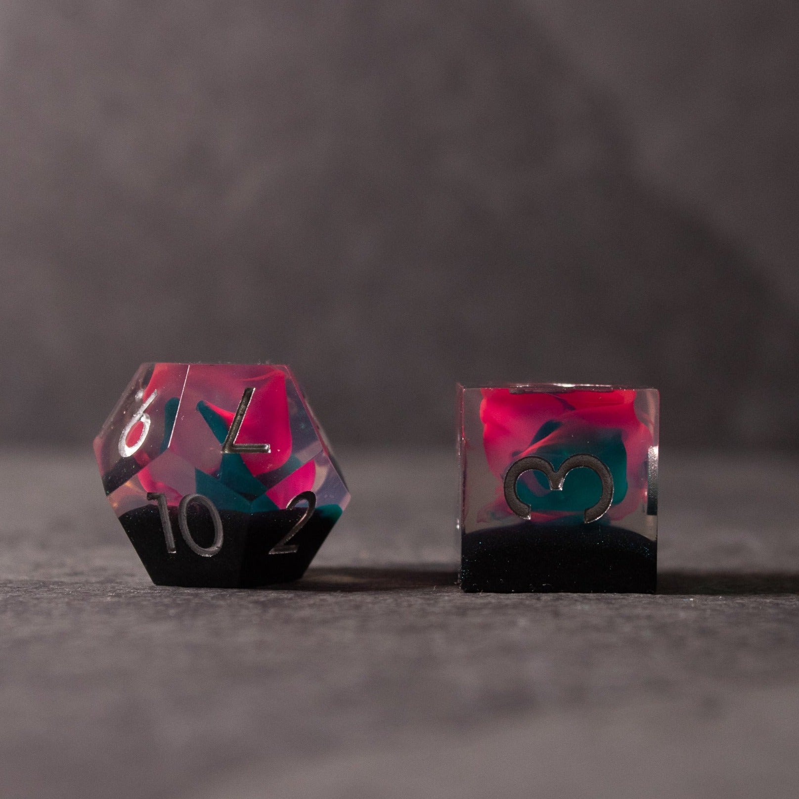 Pink & Green Flame Sharp Edge Dice Set - Pink and green translucent sharp-edged dice set with teal numbers on a dark background.