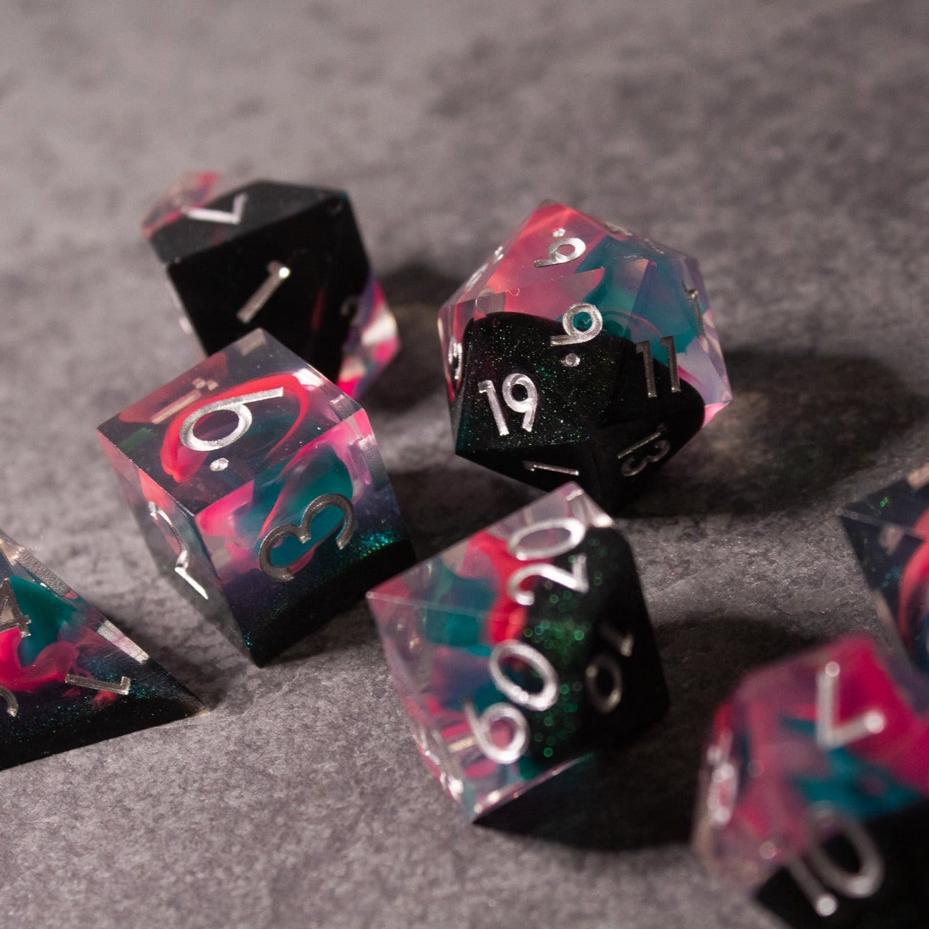 Pink & Green Flame Sharp Edge Dice Set - Set of translucent sharp edge dice with pink and green flame patterns and white numbering on gray surface.