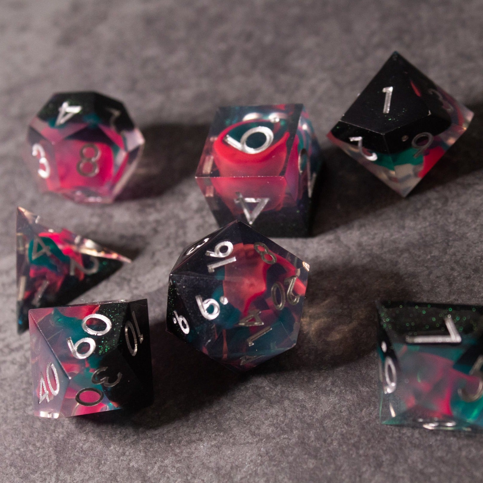 Pink & Green Flame Sharp Edge Dice Set - Seven sharp-edged polyhedral dice with pink and green swirling colors and white numbering on a gray background.