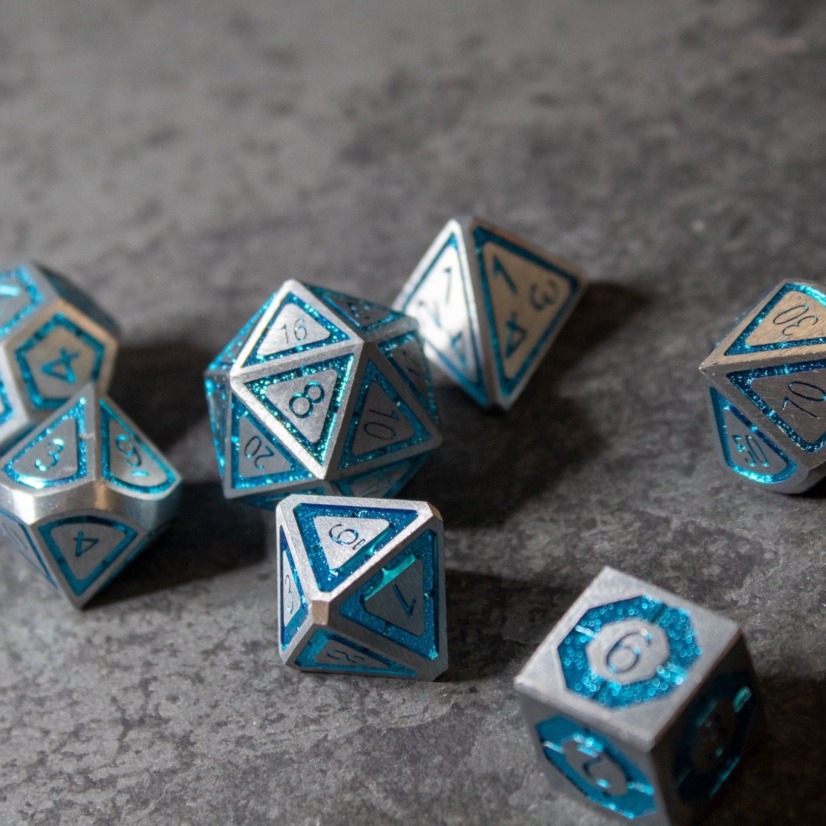 Cobalt Core Metal Dice Set - Set of blue and silver metal polyhedral dice with engraved numbers on a gray textured surface.