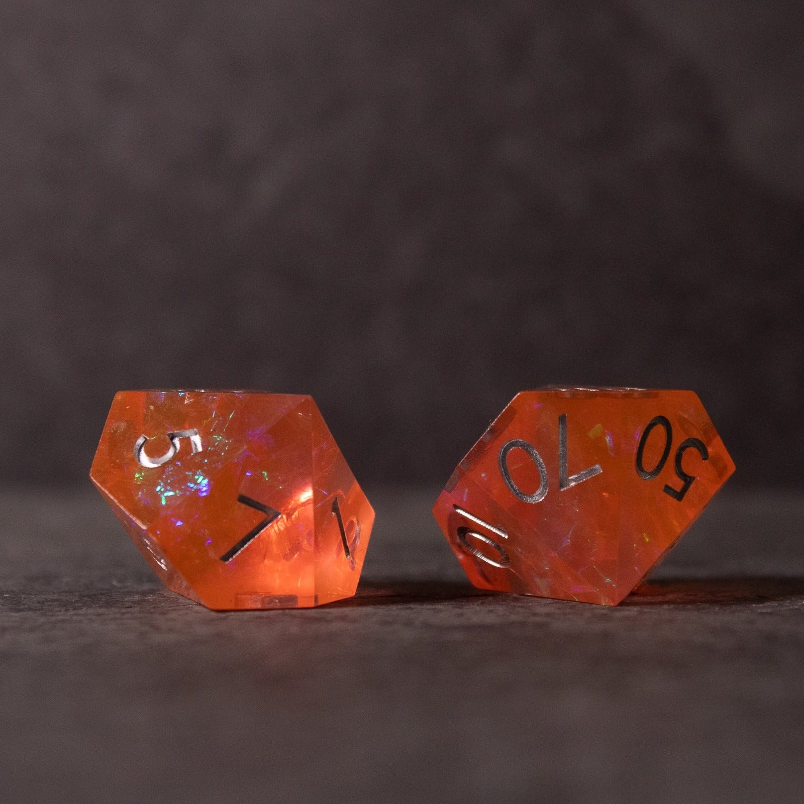 Heart Fire - Opalescent Sharp Edge Dice Set - Two translucent orange sharp-edged dice with iridescent flecks and silver numbers on a dark surface.